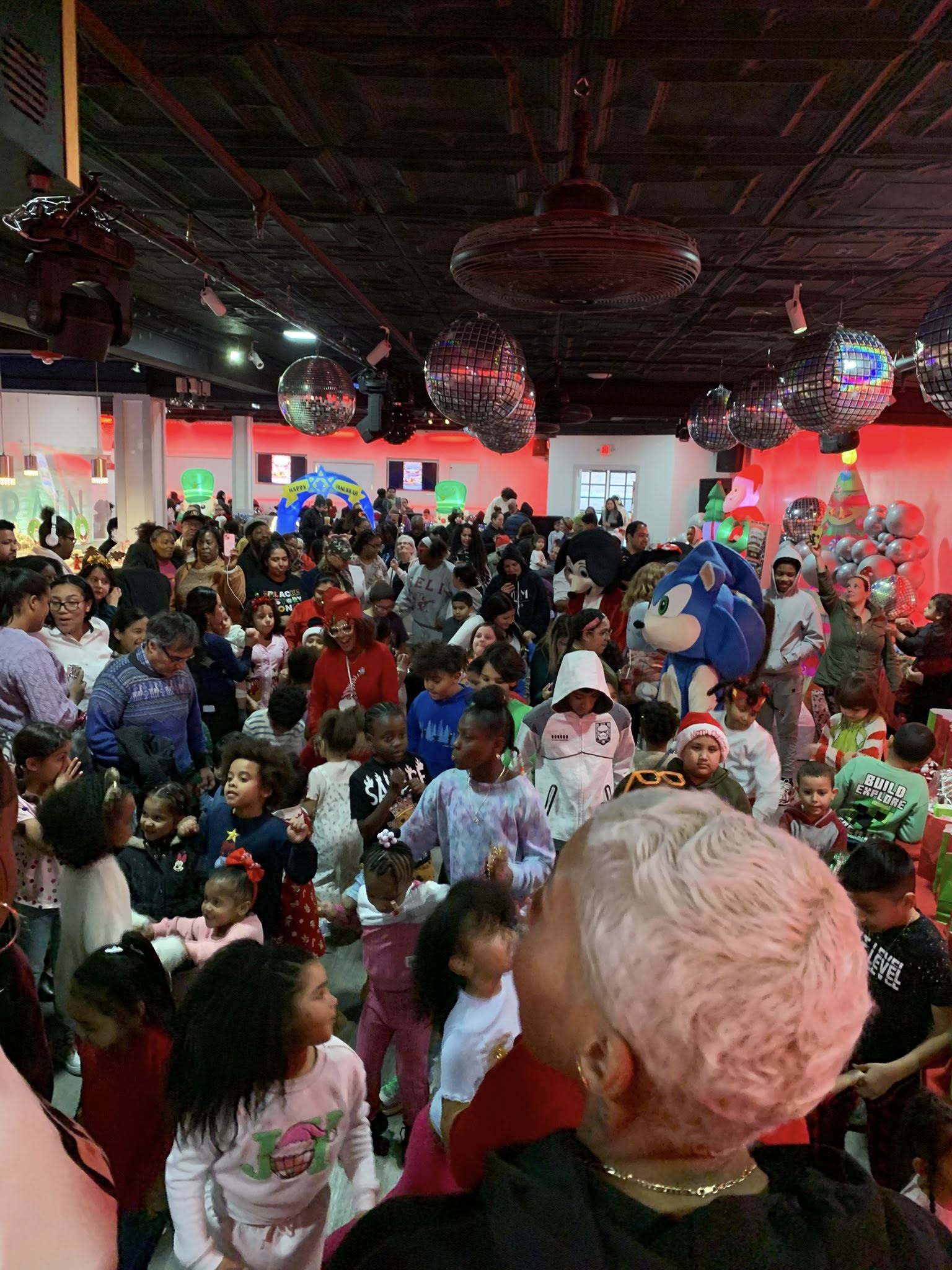 Crowd of children and adults in a decorated indoor space with disco balls and festive decorations.