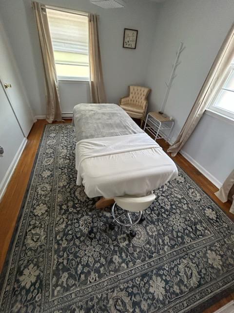 Room with massage table, window, armchair, side table, and patterned rug.