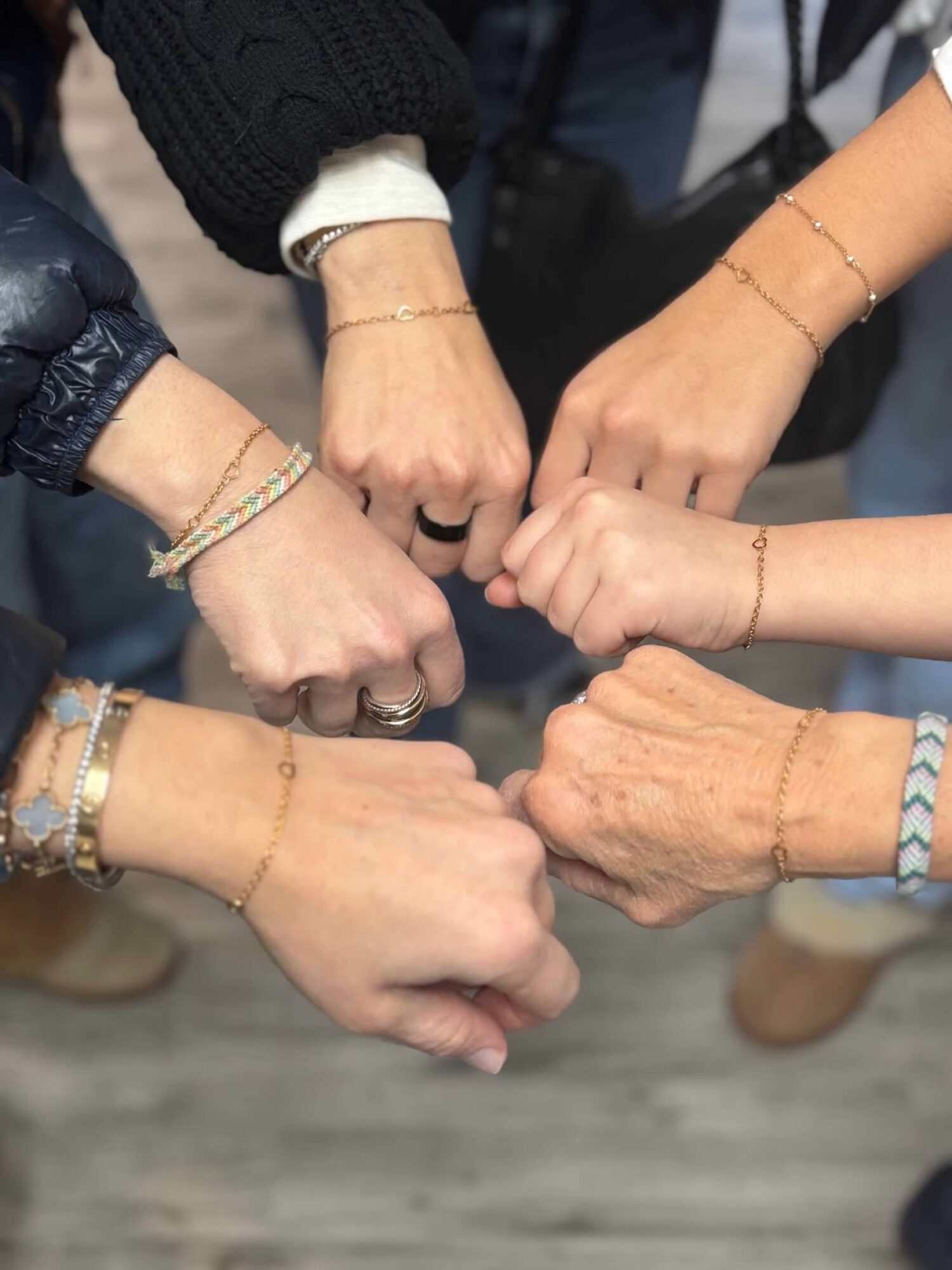 Six hands with bracelets and rings clenched into fists, showing unity and friendship.
