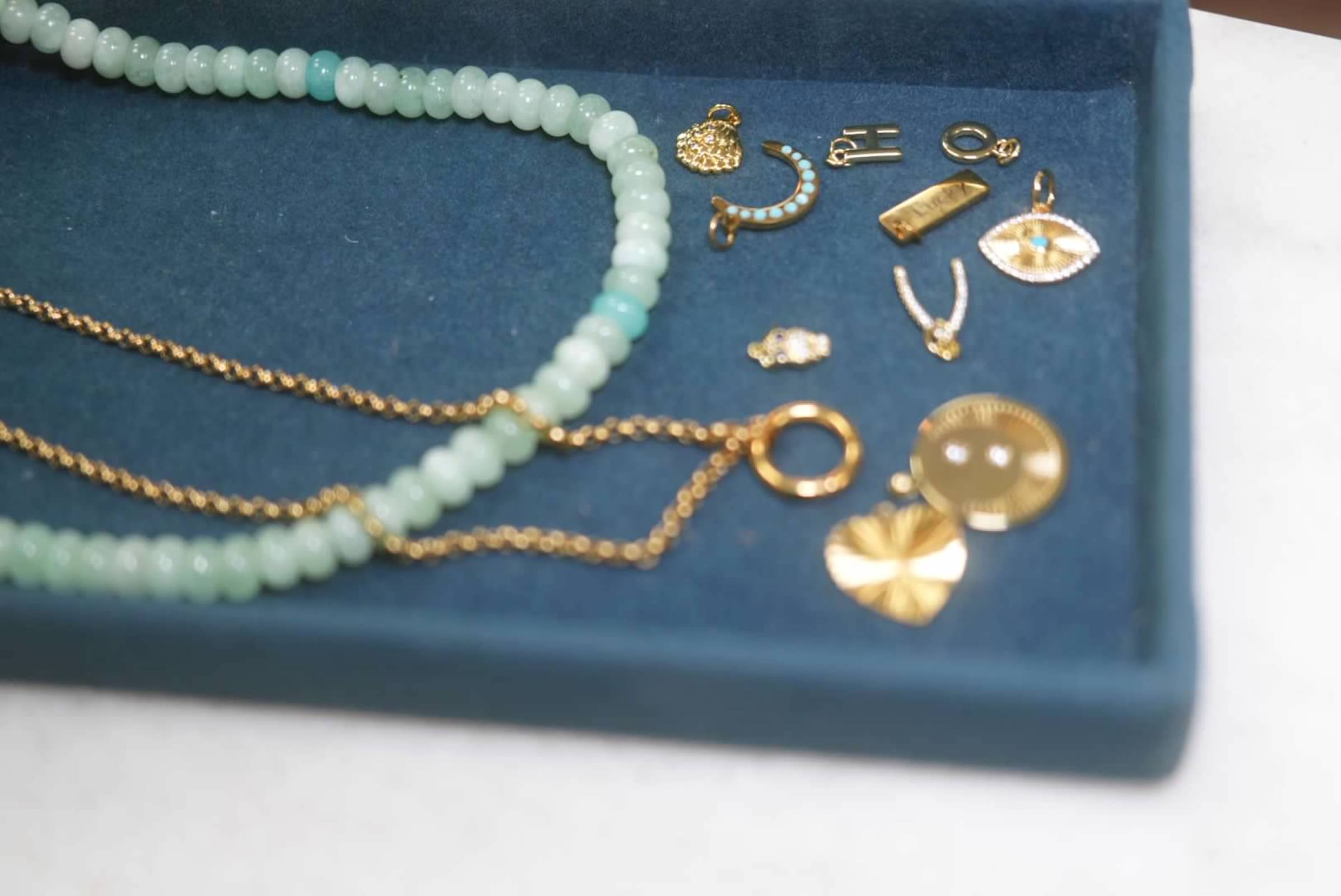 Jewelry box with necklaces and assorted earrings inside, some gold-colored and some with beads, on a blue surface.