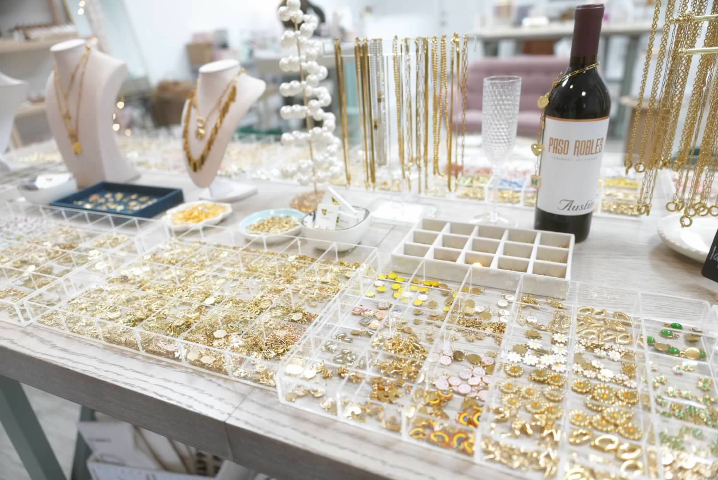 Jewelry display with necklaces, rings, and decorative items on a table, including a wine bottle and jewelry trays.