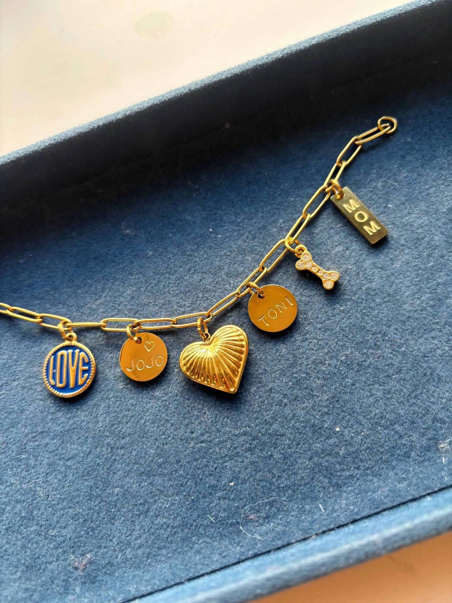 Gold bracelet with five charms including a heart, a round disc, a bone, a rectangular tag, and a circular charm with 'LOVE' engraved.