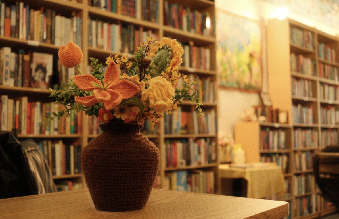 Vase with colorful flowers on a table in a library with bookshelves in background.