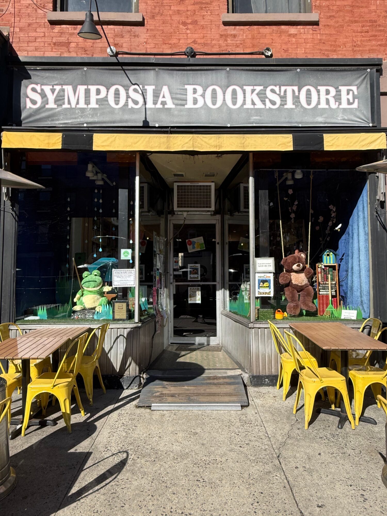 Facade of Symposia Bookstore with outdoor seating and stuffed animal figures near entrance.