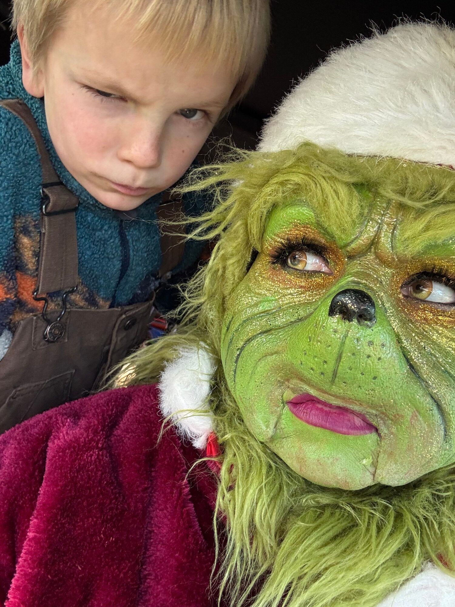 Child with a serious expression next to a person in a green furry costume with makeup and a white hat.