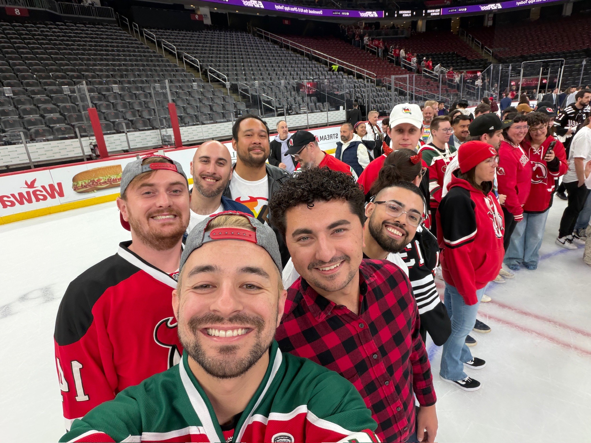Group of people standing in line on ice rink, some wearing hockey jerseys and hats, in an arena.
