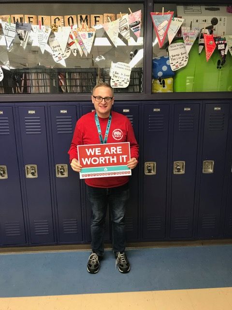Child standing in front of lockers holding a red sign that says 