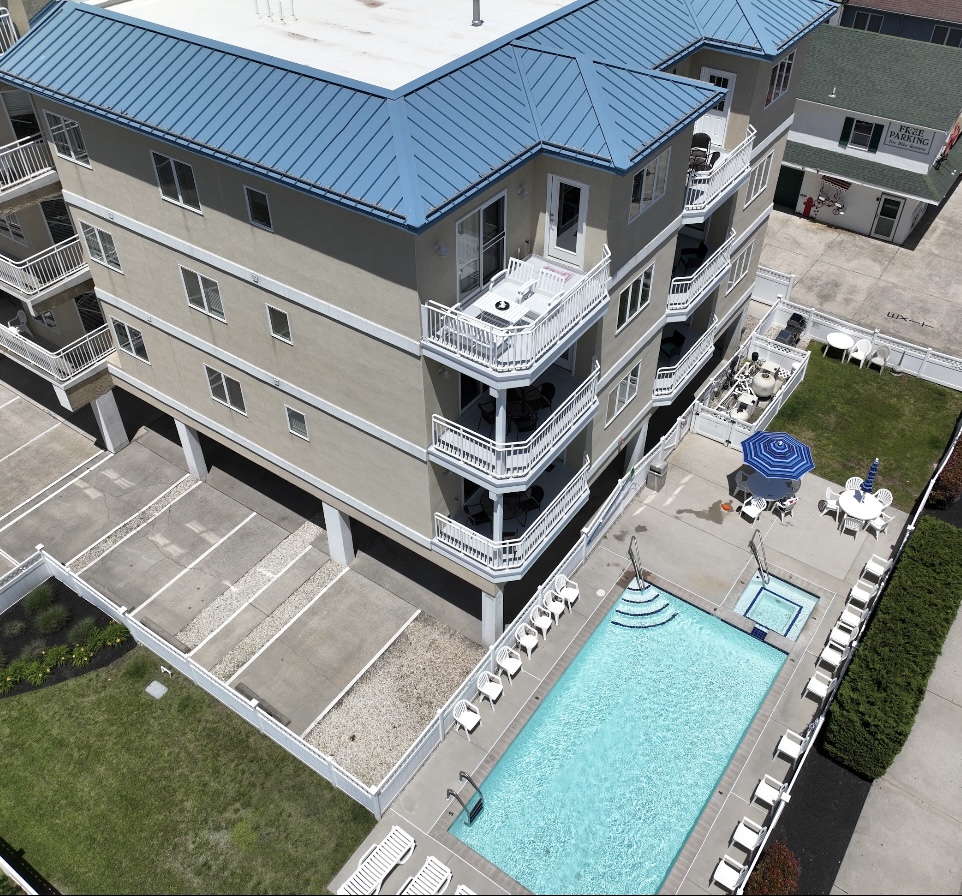 A multi-story building with balconies, a swimming pool with lounge chairs, and a small patio with an umbrella.