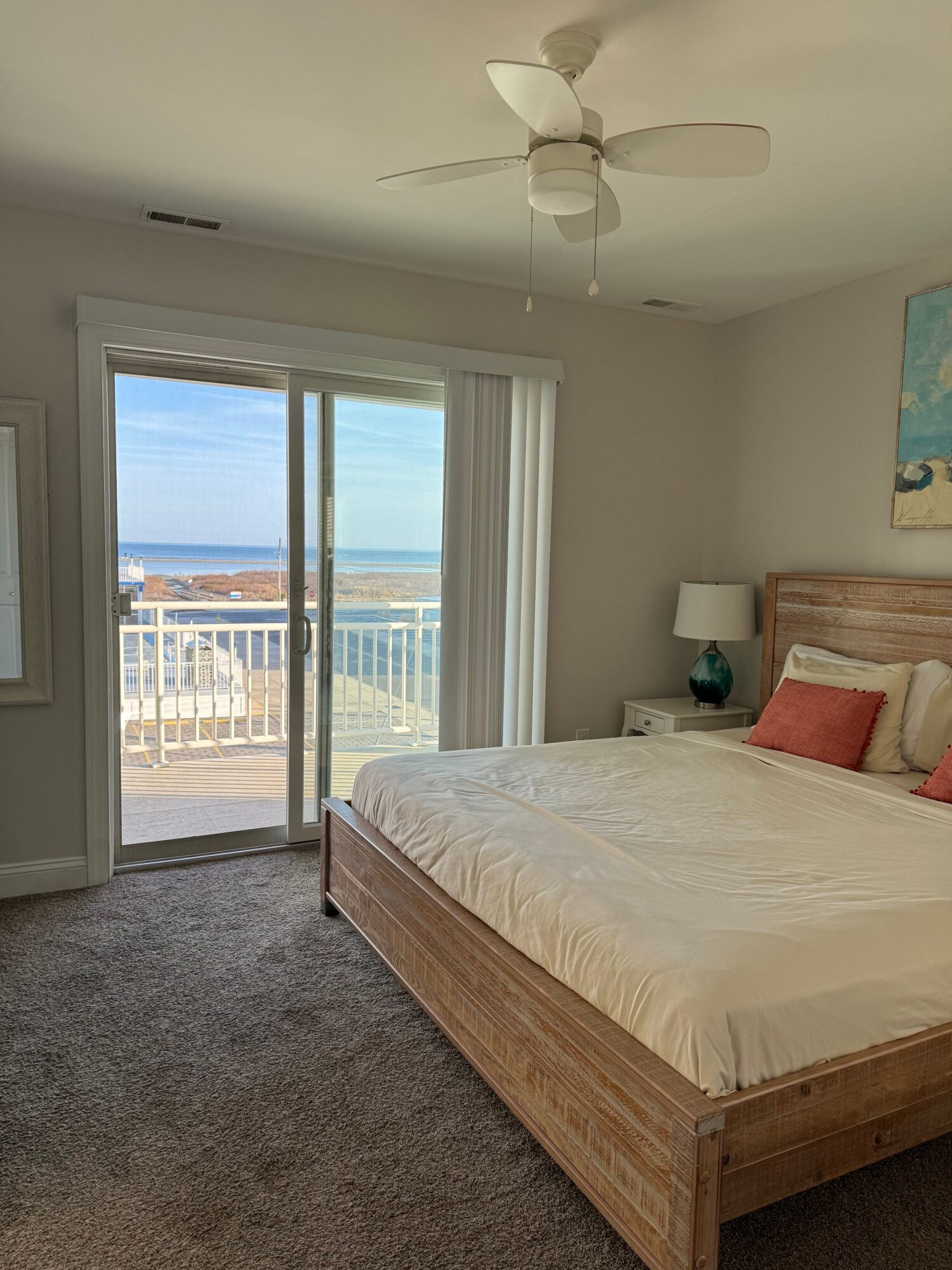 Bedroom with bed, nightstand, lamp, and sliding glass door leading to balcony with ocean view.