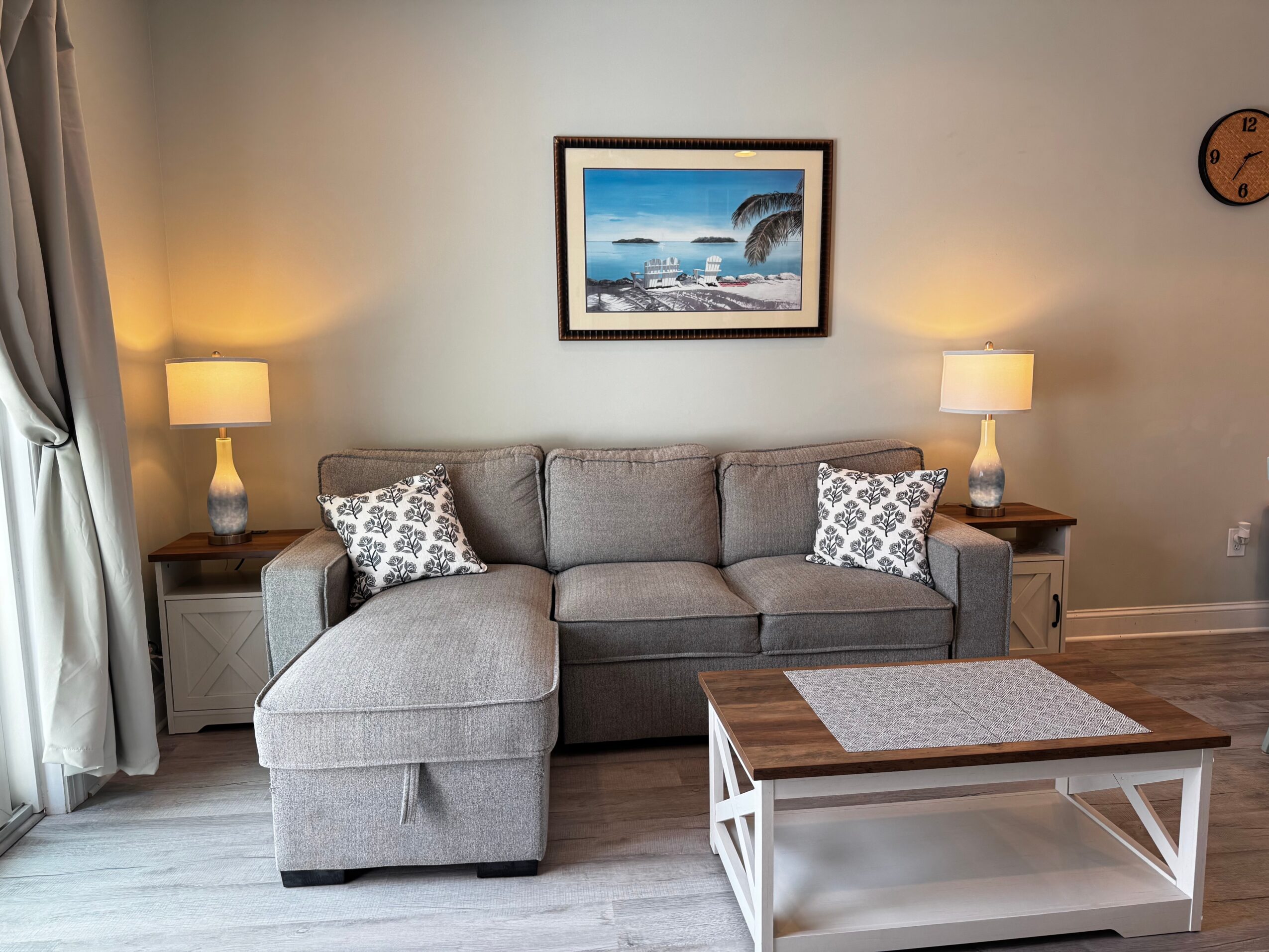 Living room with gray sofa, two side tables with lamps, framed picture above sofa, and a wooden coffee table.