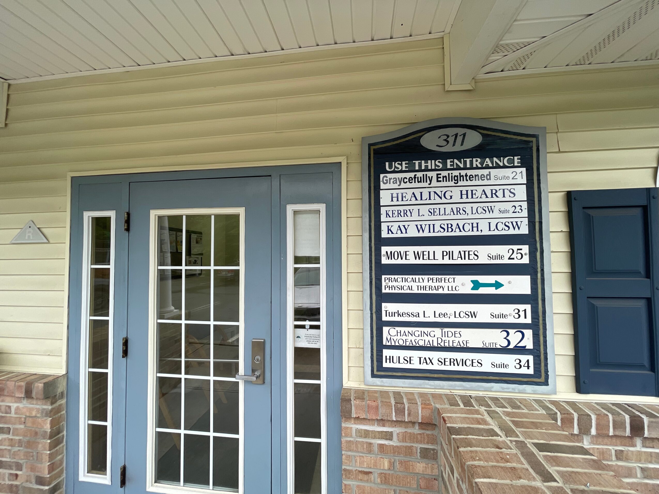 Building entrance with blue door, white trim, and a large sign listing businesses and their suite numbers.