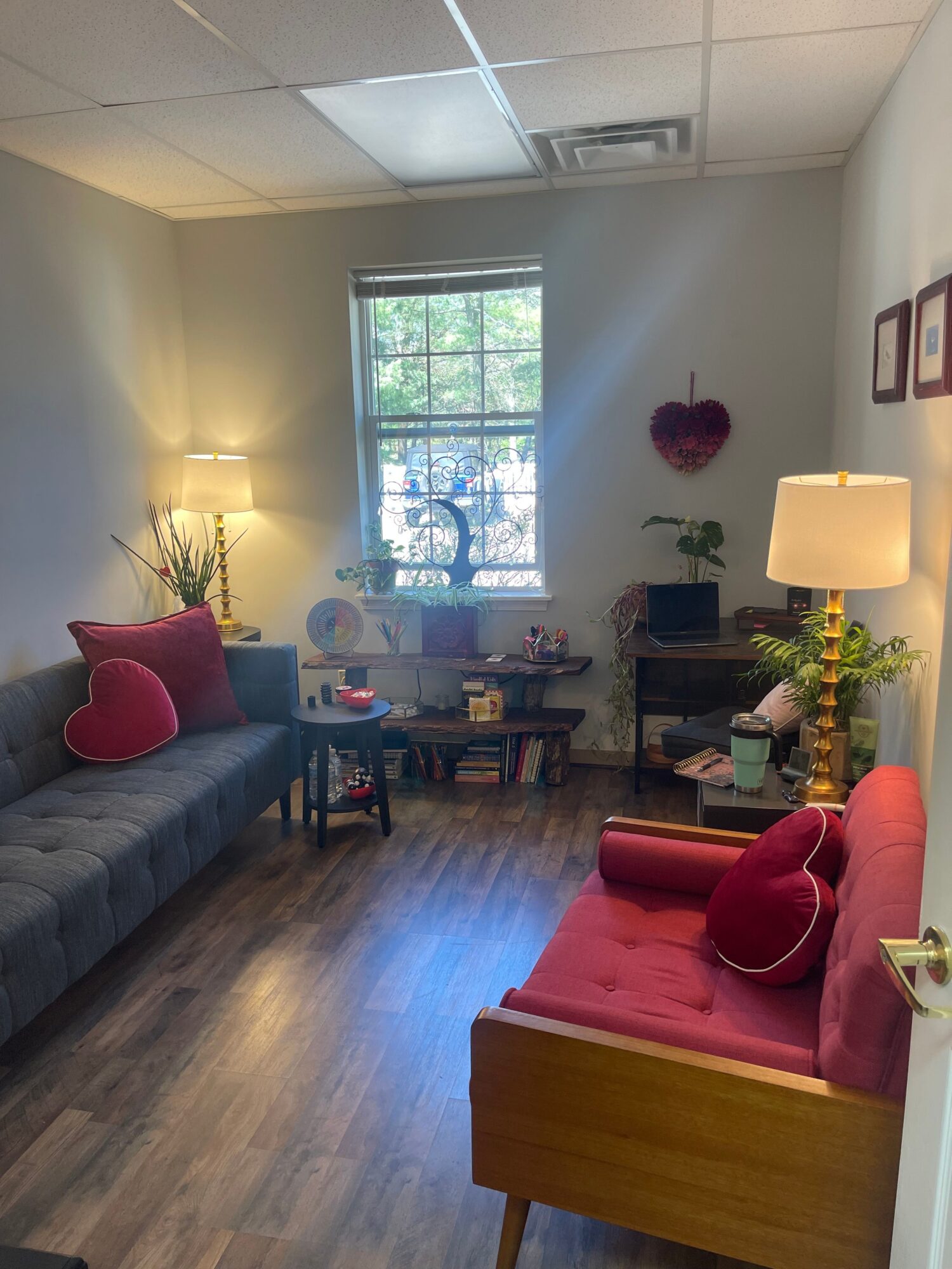 Living room with a window, sofa, armchair, lamps, and wall decorations, hardwood floor, and a small table.