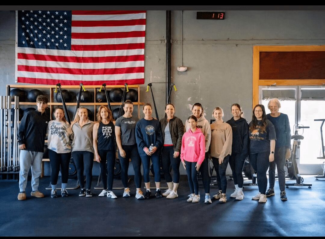 Group of people standing in a gym with an American flag on the wall behind them.