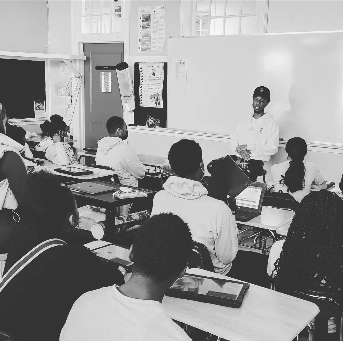 Teacher standing at whiteboard in classroom with students seated at desks using tablets.