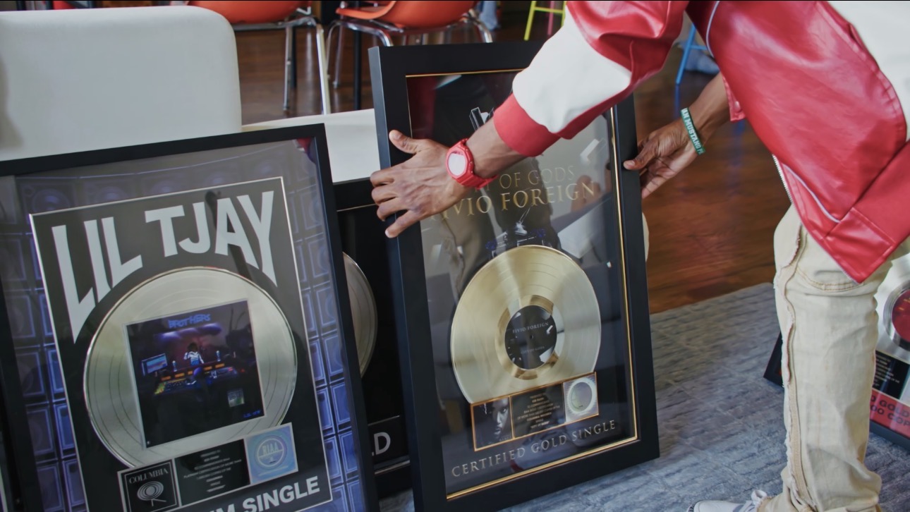Person in red jacket adjusting framed gold record awards on display.