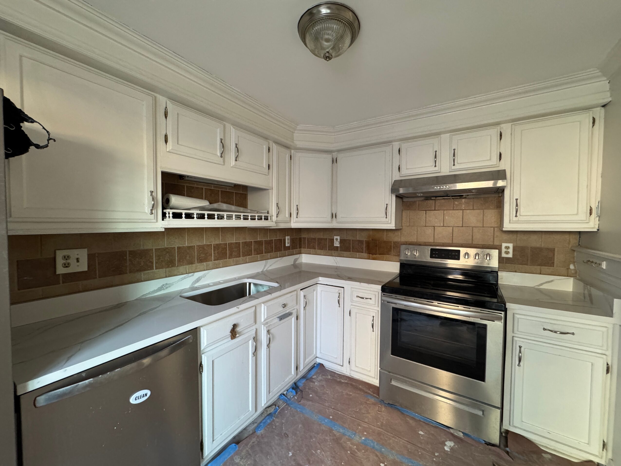 Kitchen with white cabinets, brown tile backsplash, stainless steel stove, and a ceiling light fixture.