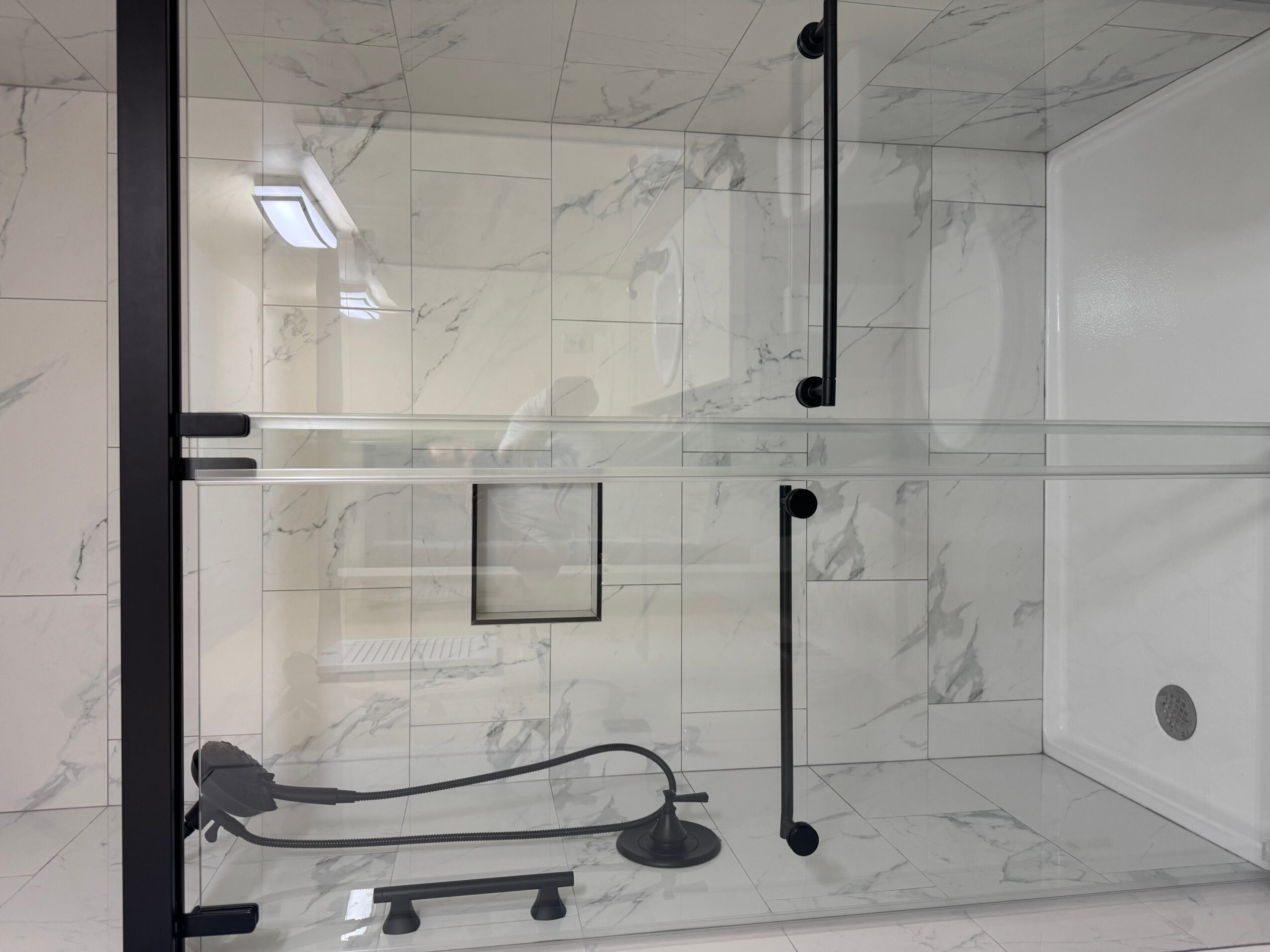 Shower area with glass door, marble walls, and a showerhead, viewed from outside the shower.