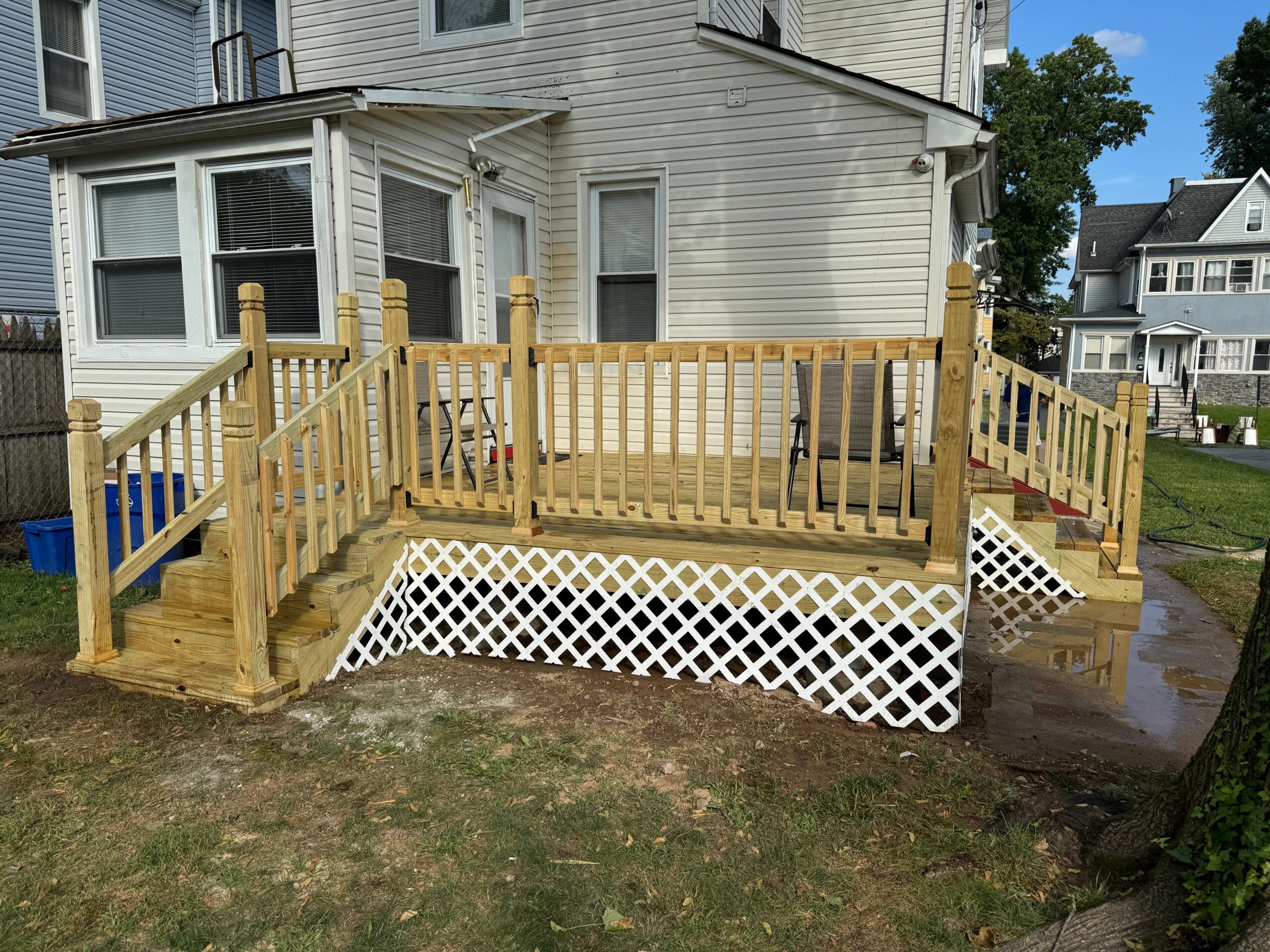Wooden deck with railing attached to a white house, with lattice skirting and a grassy yard in the foreground.