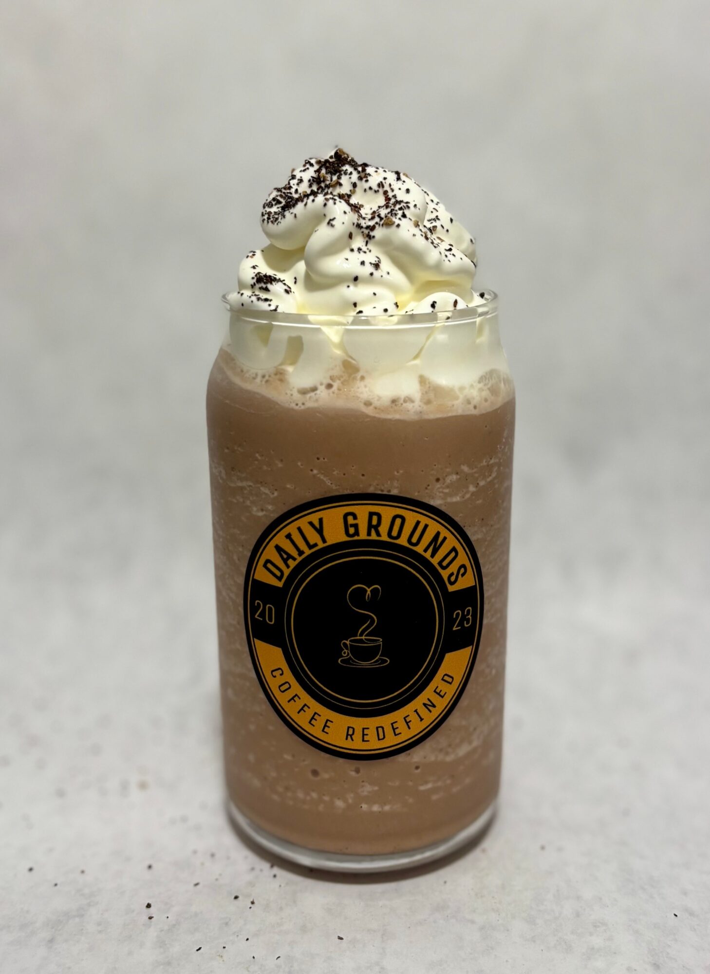 Chocolate drink in a jar with whipped cream and sprinkles, labeled Daily Grounds Coffee Medellín, on a light background.