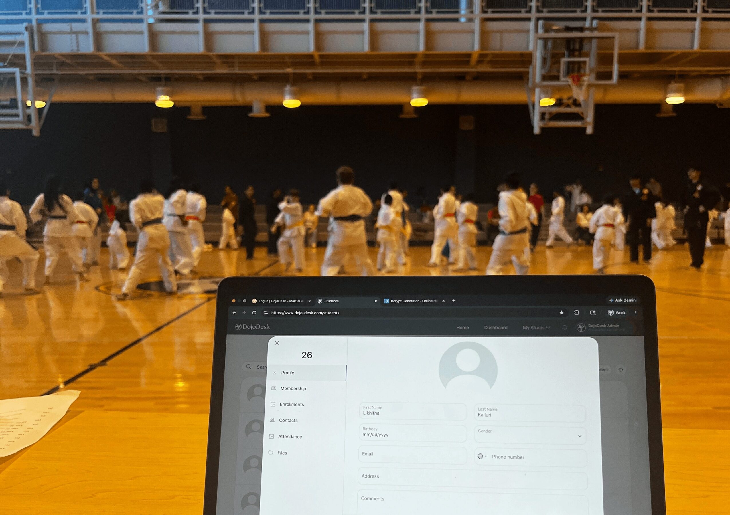 Indoor martial arts class with students in white uniforms practicing on a wooden floor, viewed from a tablet screen.