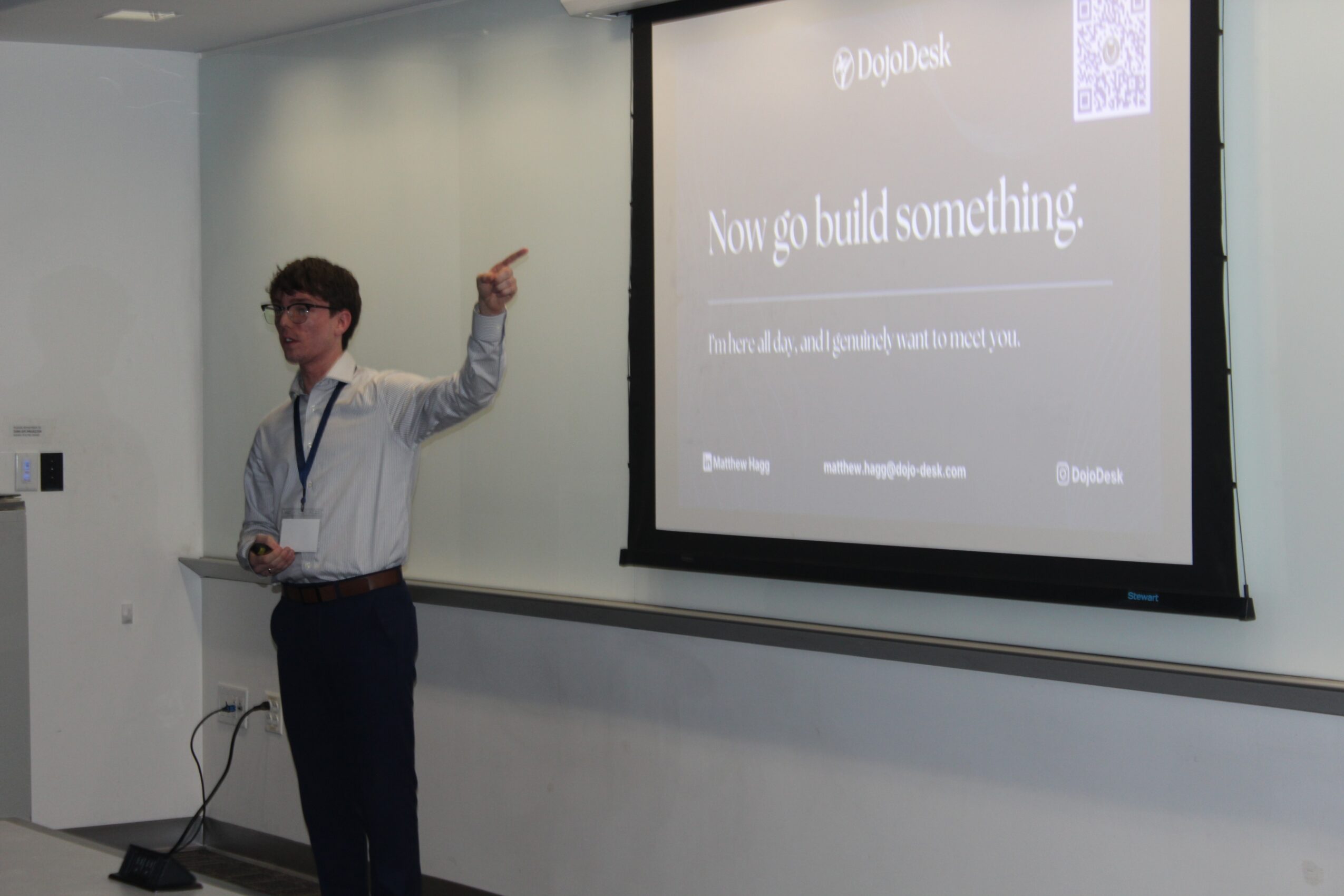 Young person in glasses and striped shirt points at a presentation slide in a classroom.