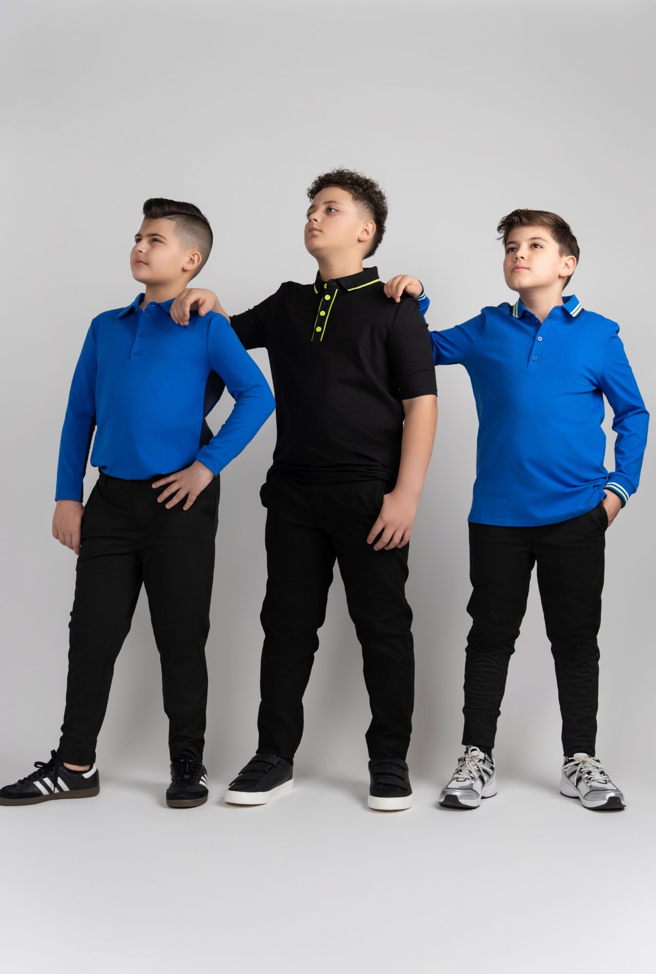 Three boys standing side by side, each with one arm on the other's shoulder, against a plain background.
