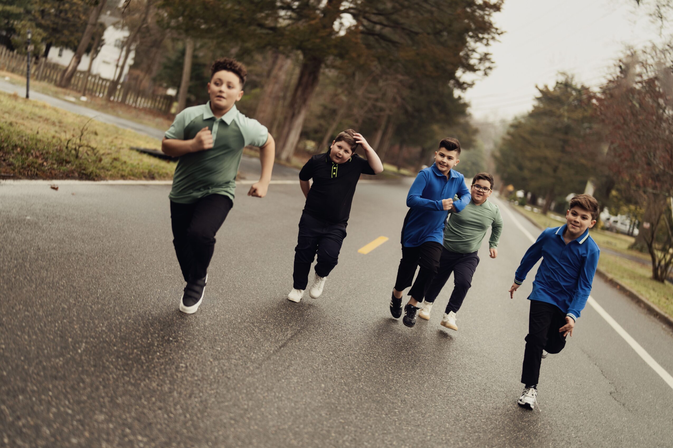 Group of five people walking on a road with trees in the background, some waving and smiling.