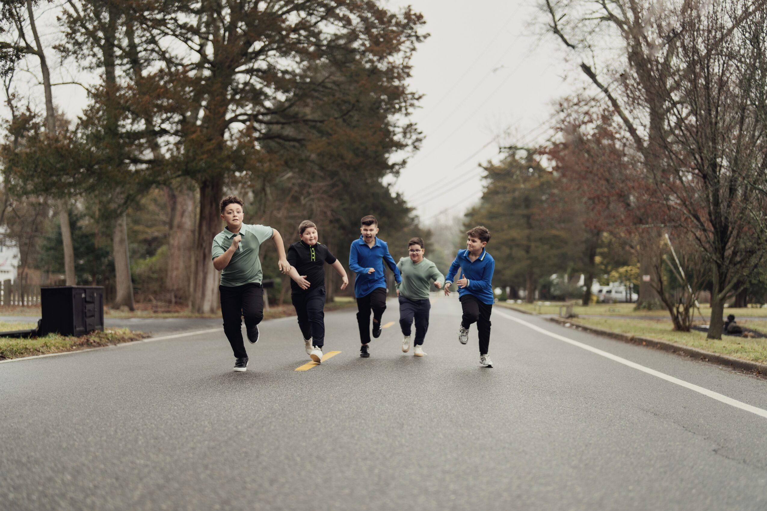 Five people running on a suburban street with trees and houses in the background.