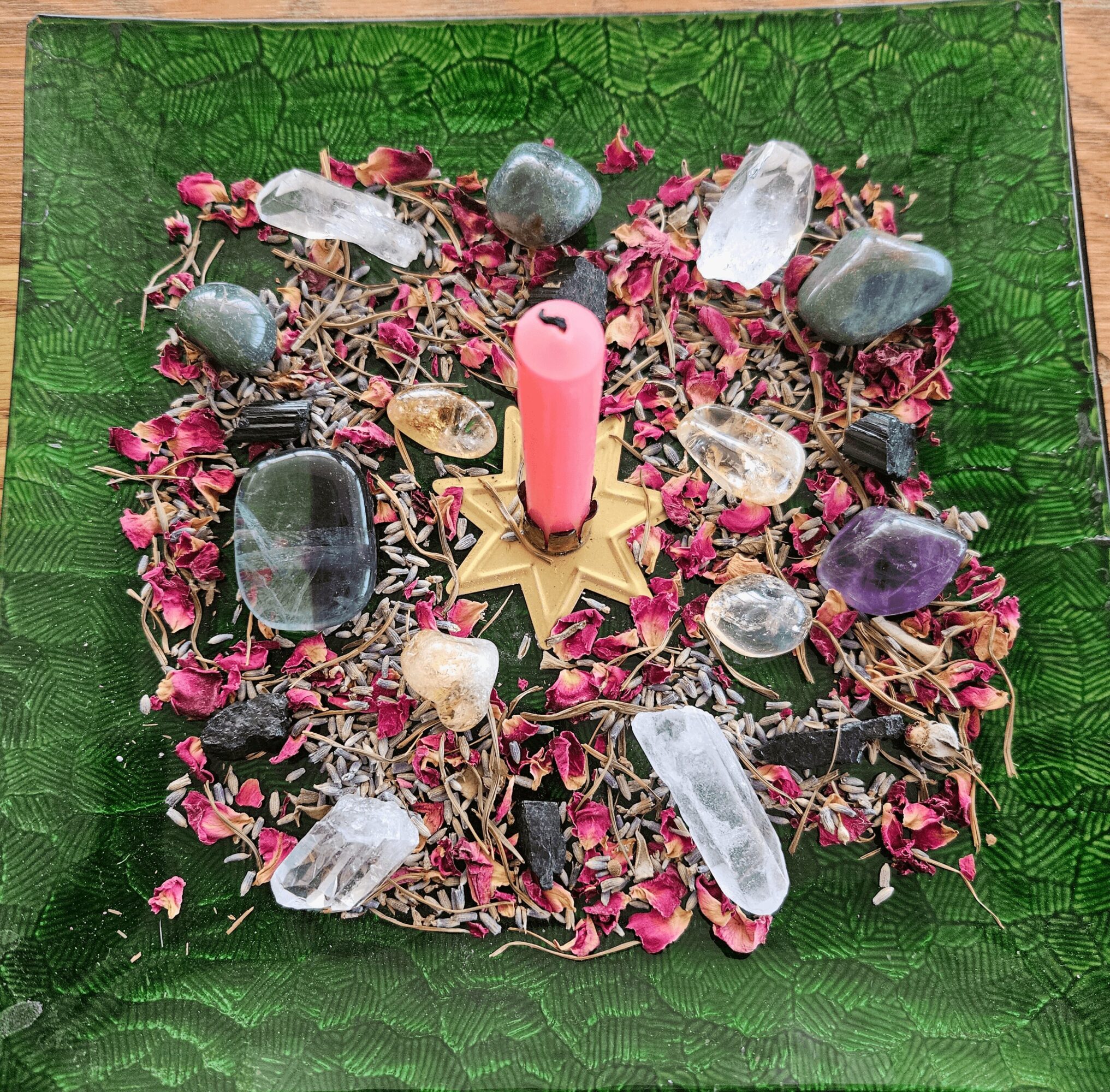 Decorative arrangement with crystals, stones, dried flowers, a pink candle, and a star-shaped base on a green textured tray.