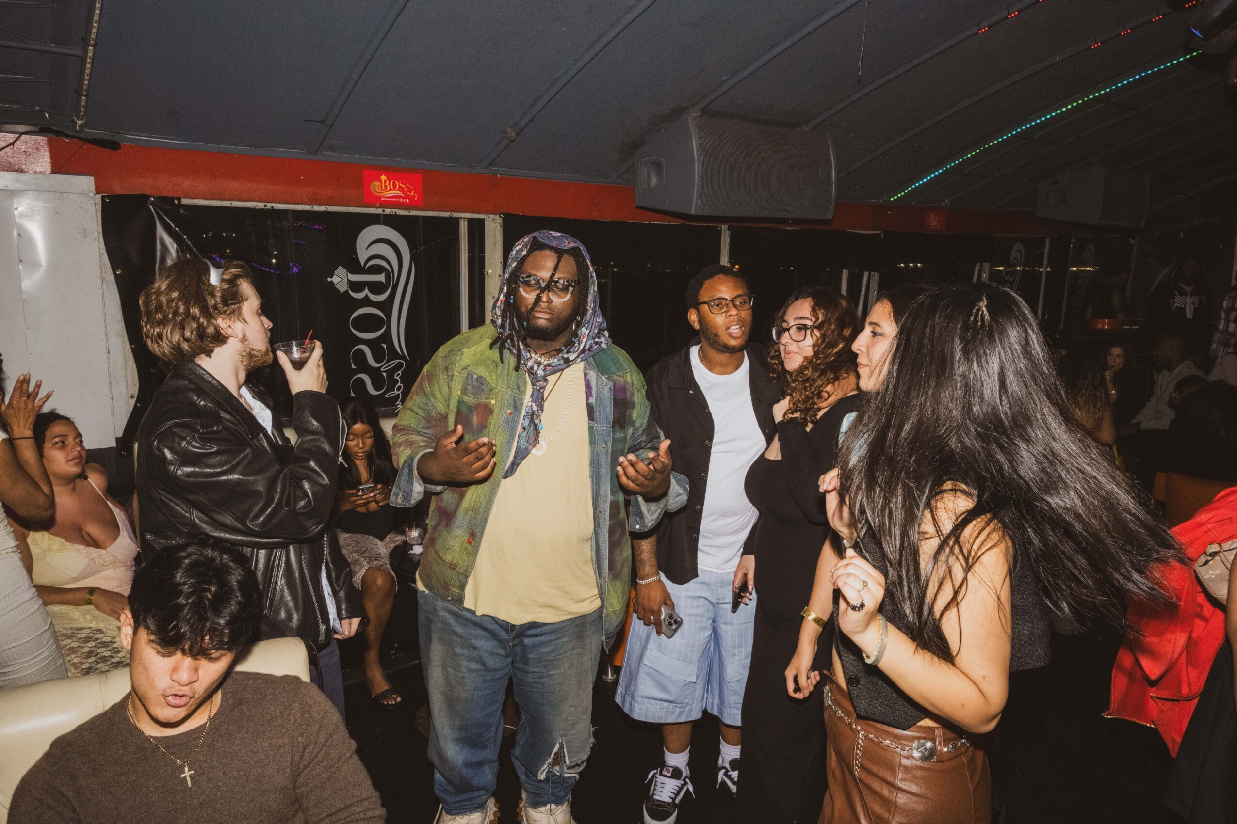 Group of people socializing indoors, some talking and others listening, with a dark ceiling and dim lighting.