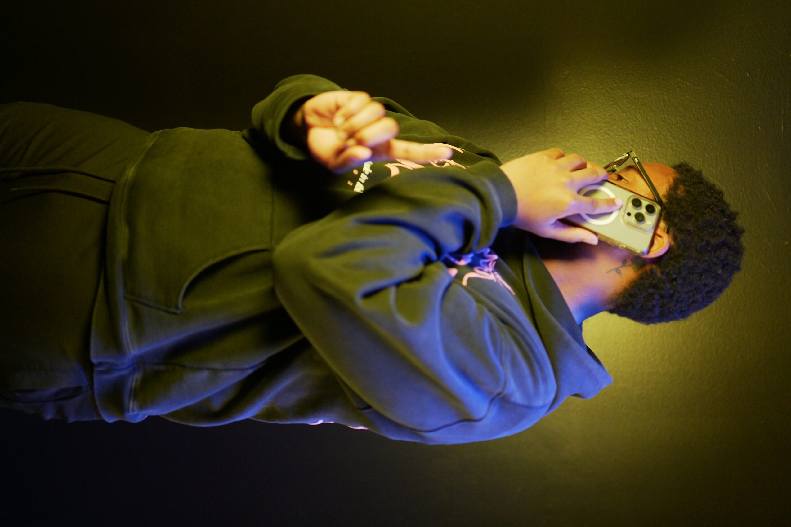 Person holding a vintage radio, wearing a dark hoodie, with a dark background.