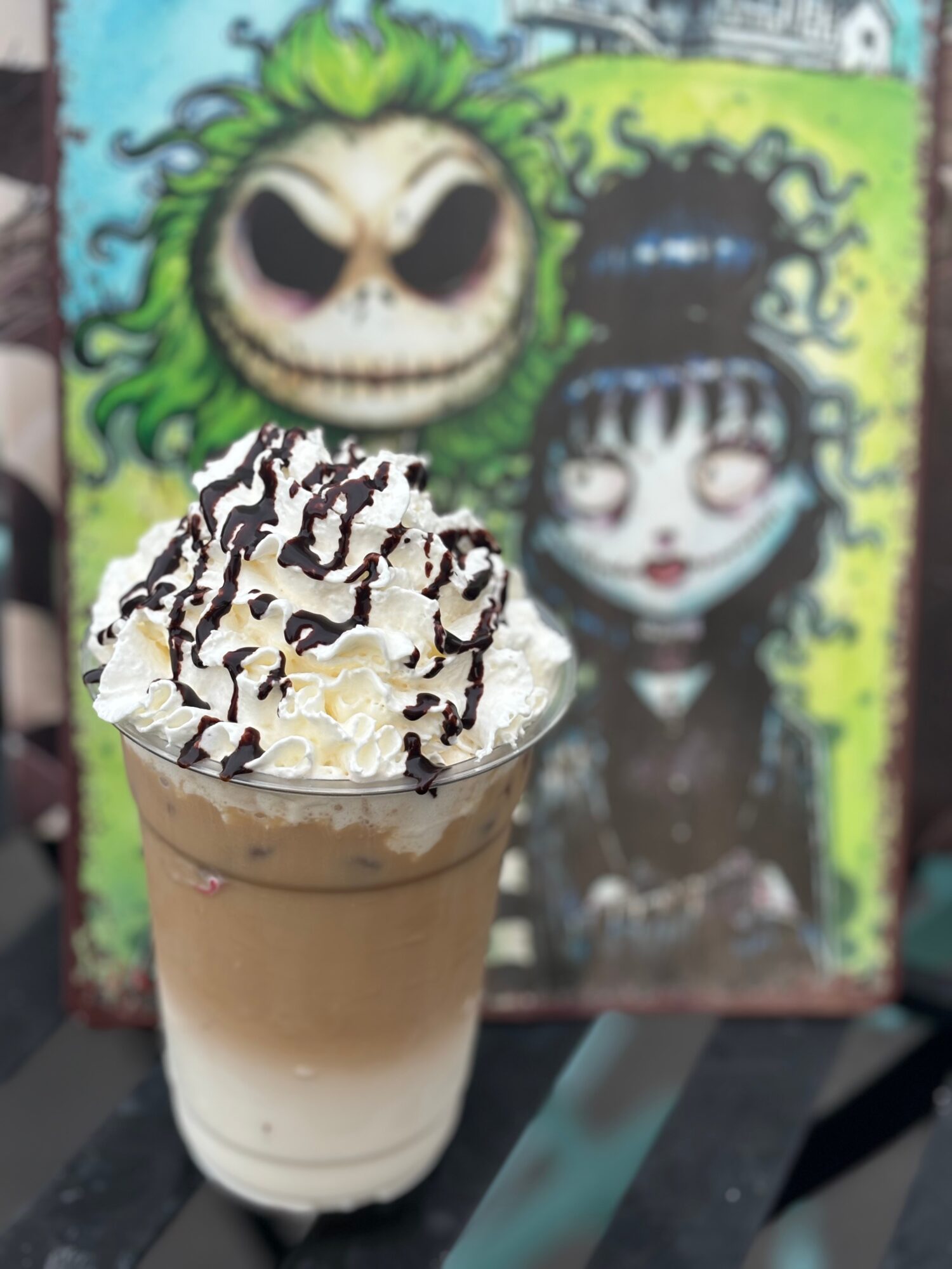 Whipped cream-topped coffee drink with chocolate drizzle in front of colorful animated character poster