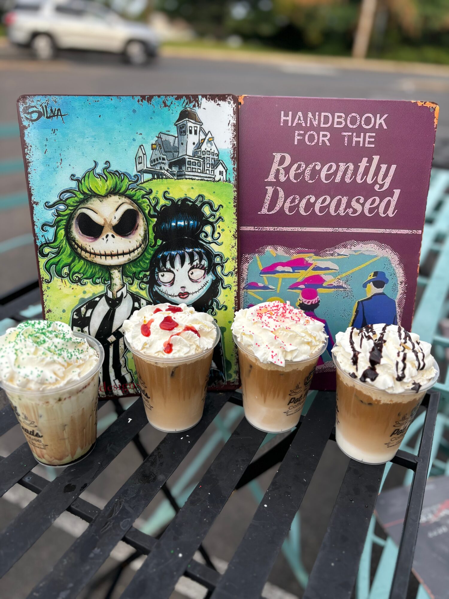 Four cupcakes with various toppings in front of two books, one titled 'Handbook for the Recently Deceased' and the other with a colorful illustration.