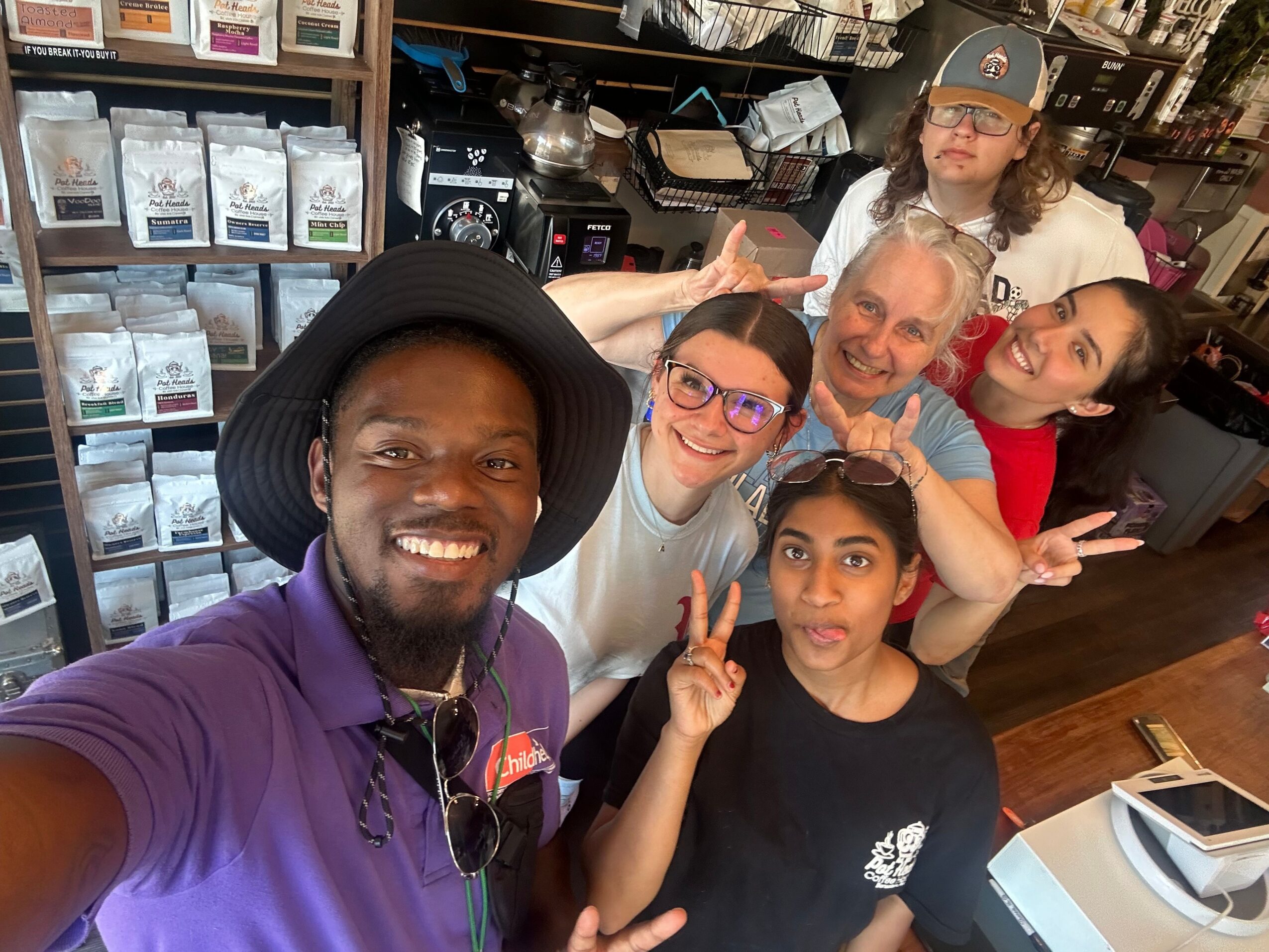 Group of six people smiling and making peace signs in a store with shelves of products behind them.