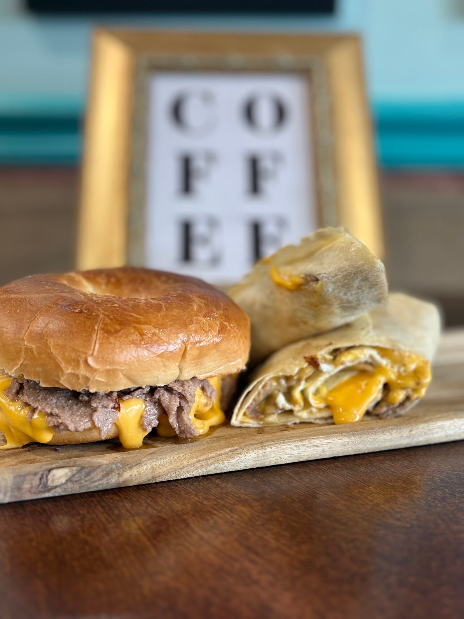 A cheeseburger with a bun, meat patty, and melted cheese, alongside two potato chips with cheese filling, on a wooden surface.
