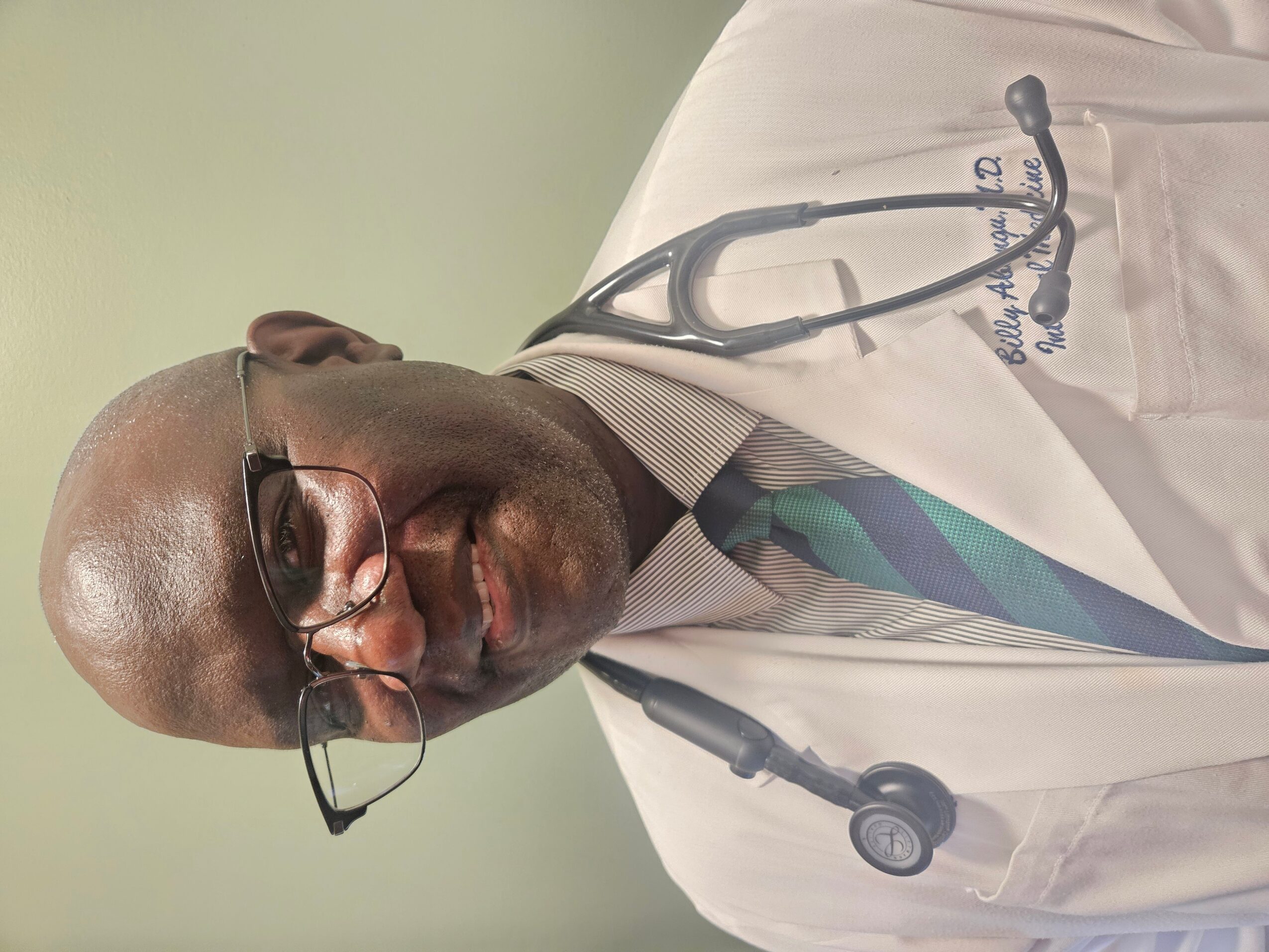 A male doctor wearing glasses, a white coat, and a stethoscope around his neck, smiling at the camera.