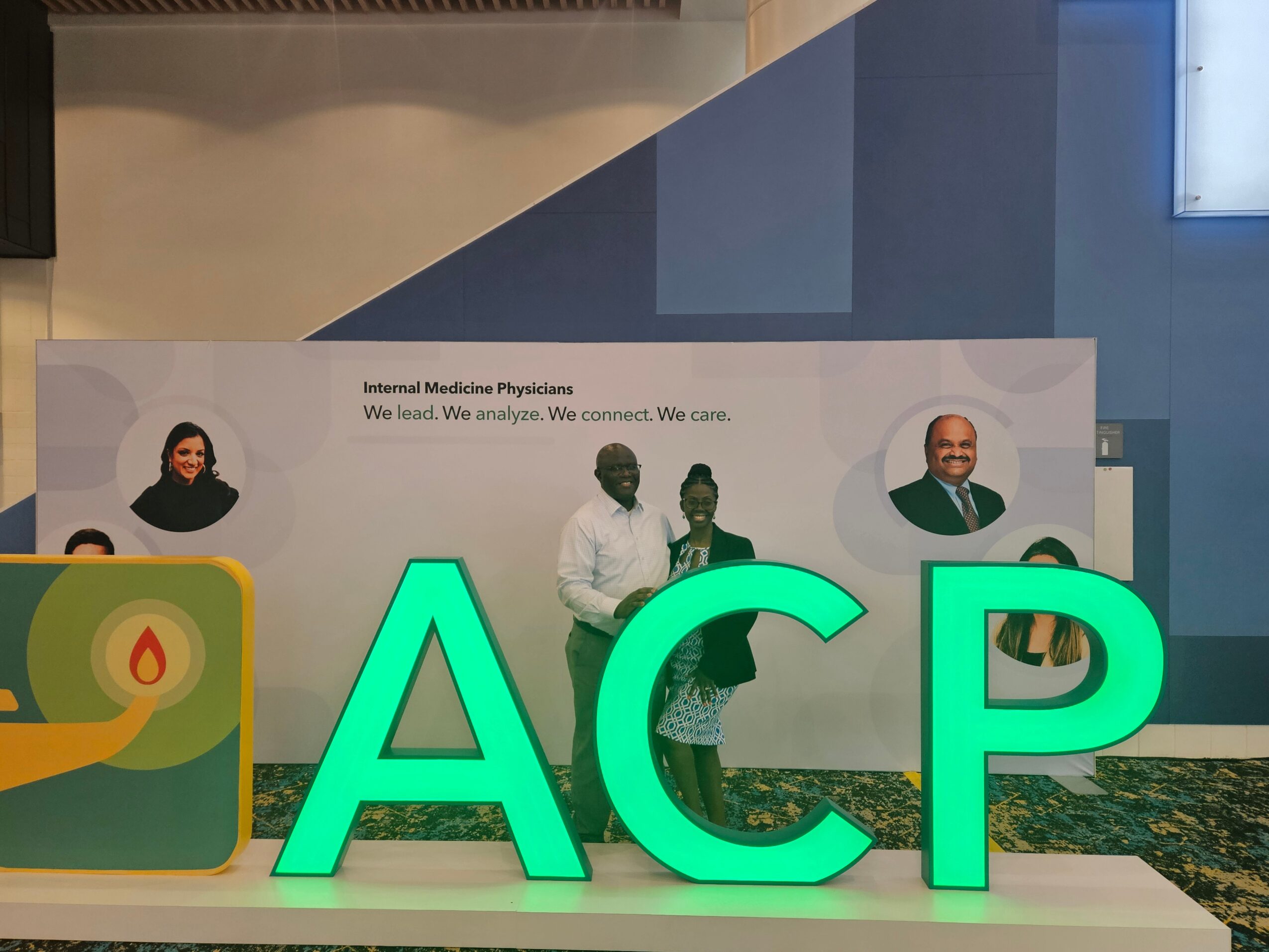Three people standing in front of a medical-themed display with large illuminated letters 'ACP'.