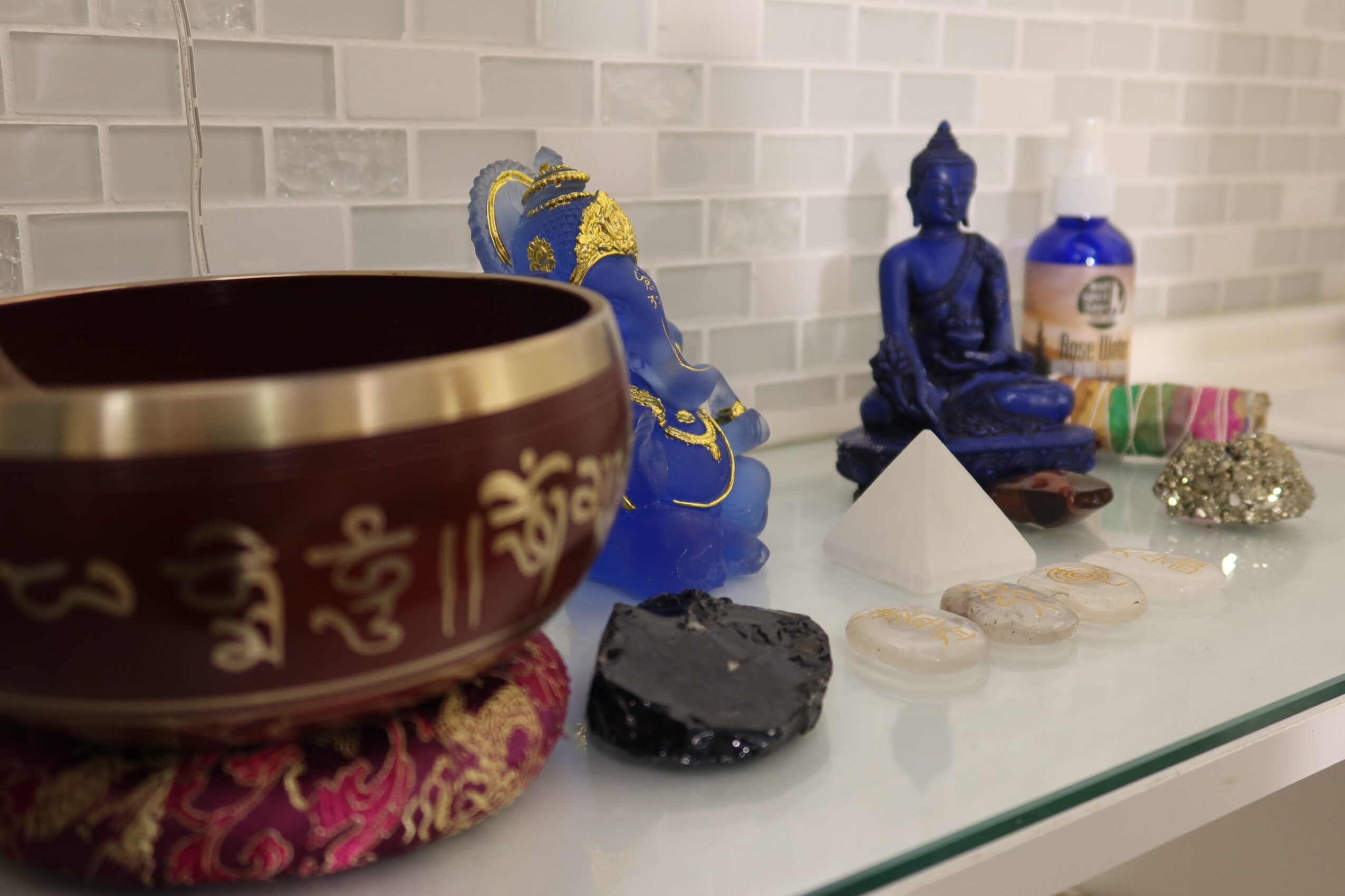 A glass shelf with a singing bowl, a black stone, a blue Buddha statue, and various bottles and objects.