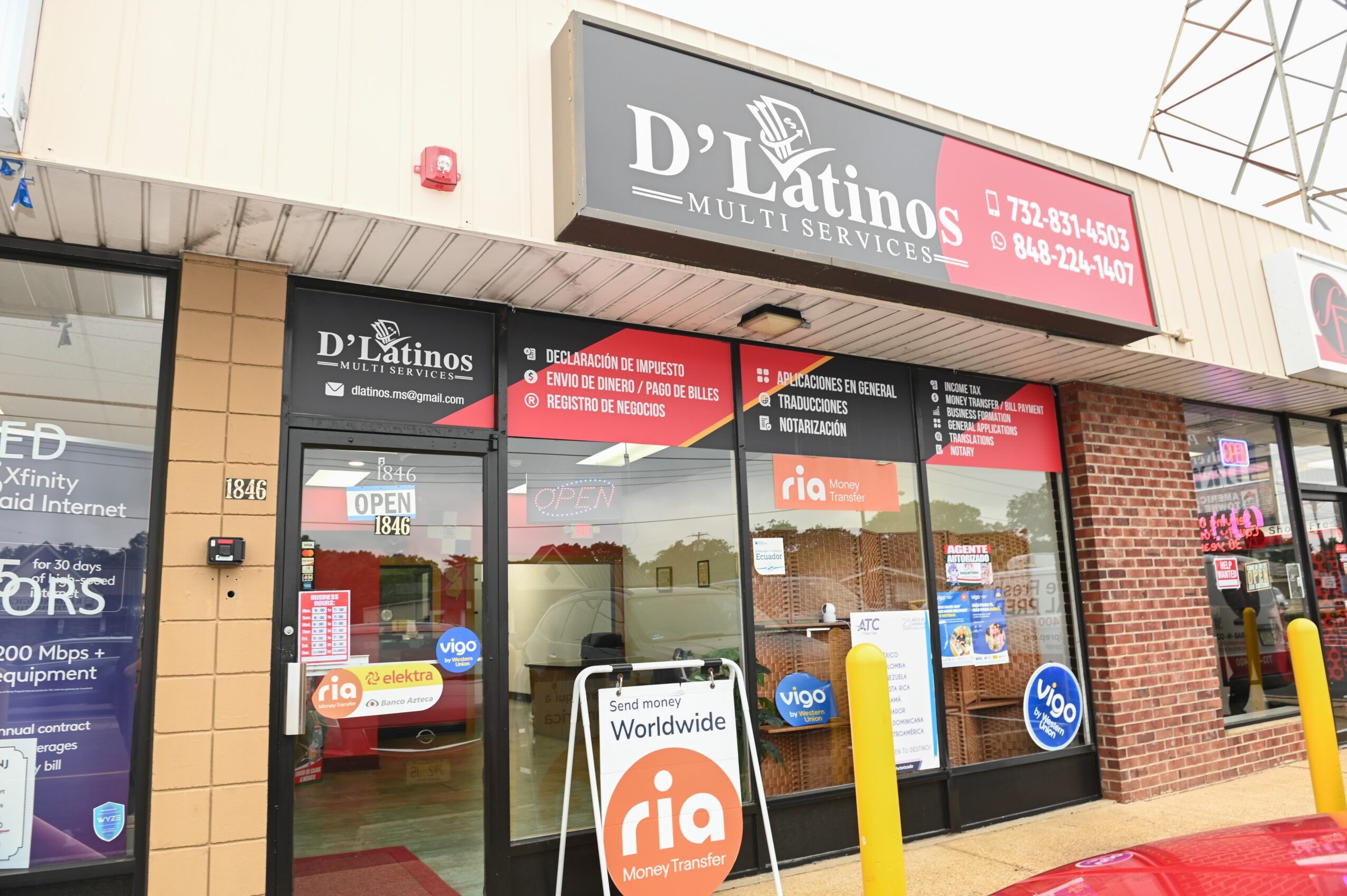storefront with signs for D'Latinos and Ria, glass doors, and yellow bollards outside, with a sidewalk and building exterior