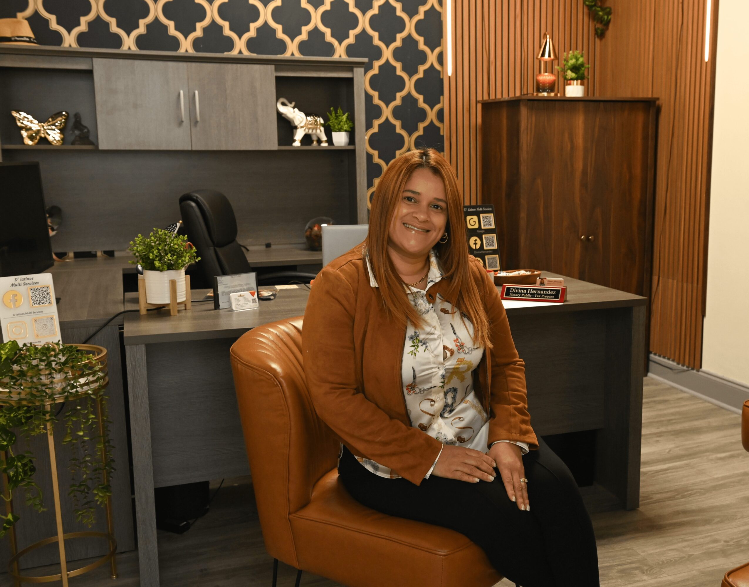Woman sitting on a chair in an office with a desk, shelves, and decorative items behind her.