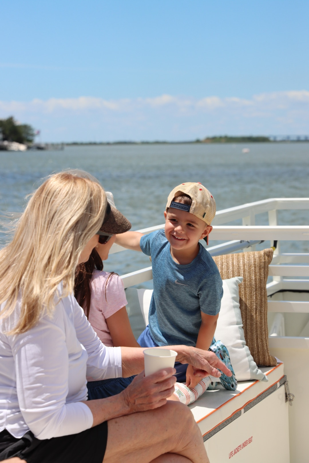 Child smiling and touching an adult's head on a boat with water and sky in background.