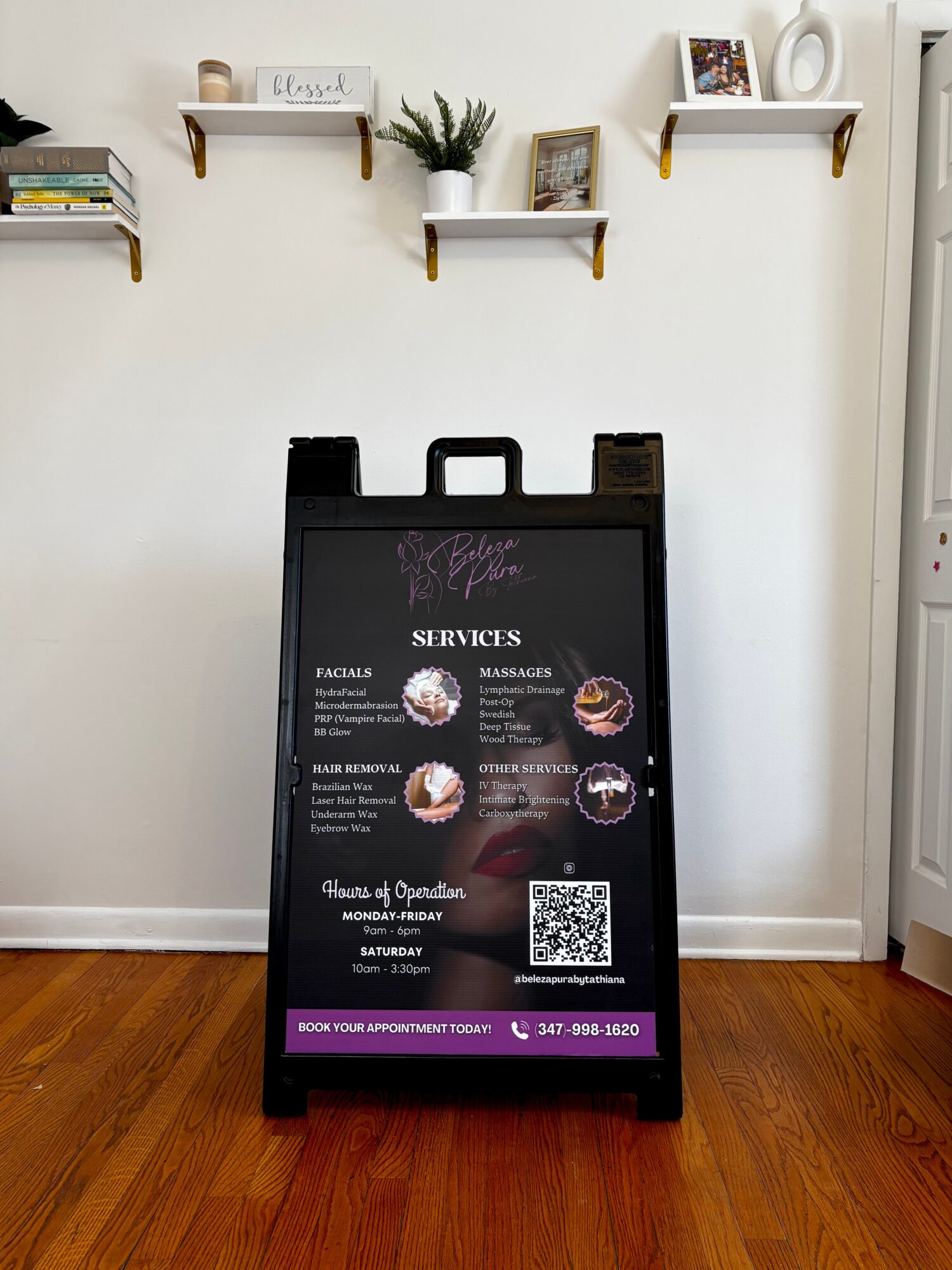 A black A-frame signboard displays services and a QR code, positioned on a wooden floor against a white wall with shelves.
