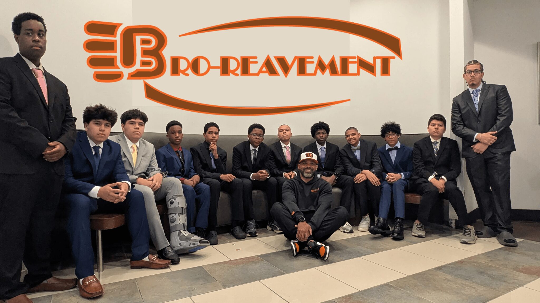 Group of people sitting and standing in front of a wall with a logo and text, some wearing suits and casual clothing.