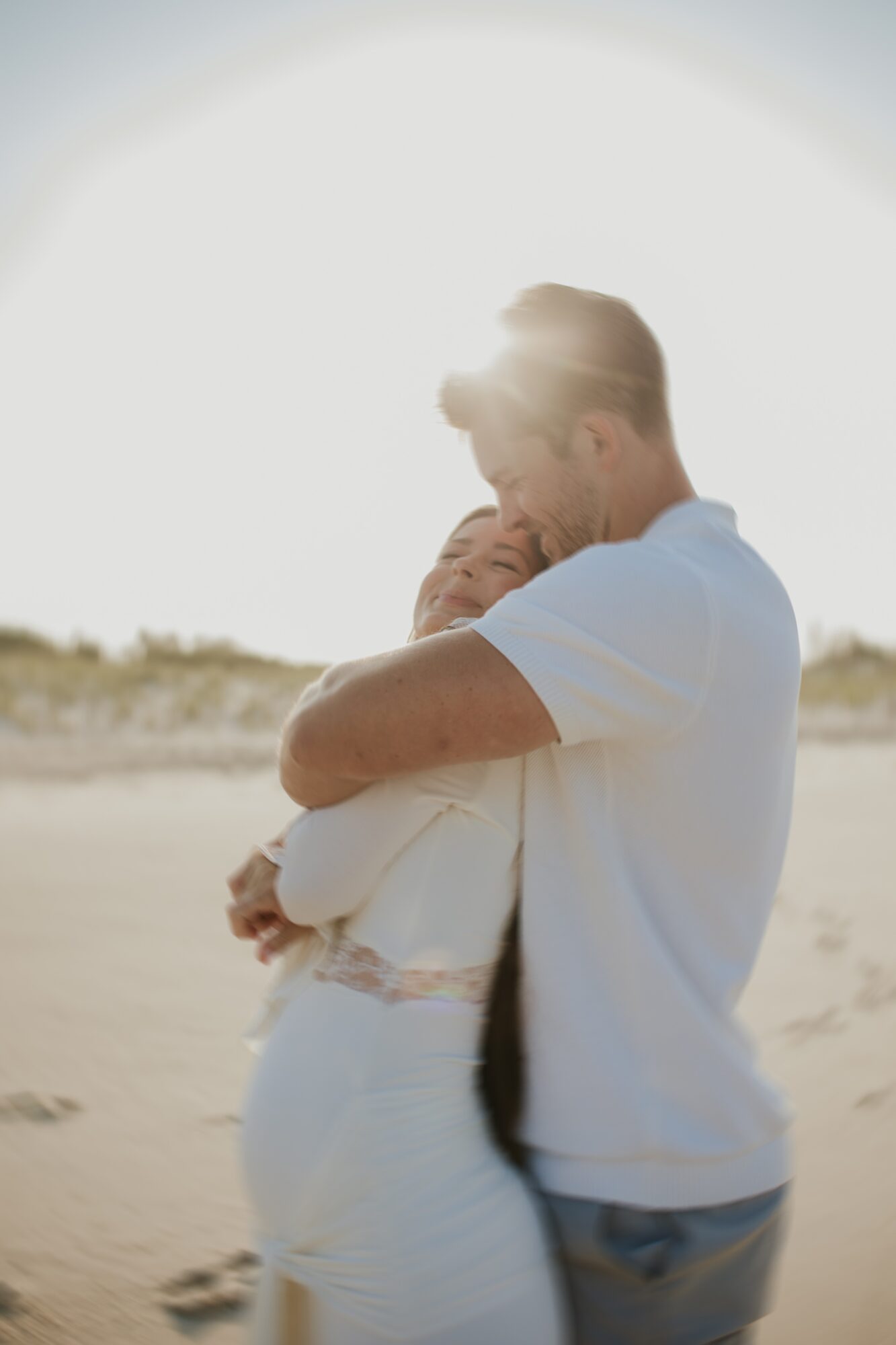 Man holding a child on a beach with bright sunlight behind them, both facing each other and smiling.