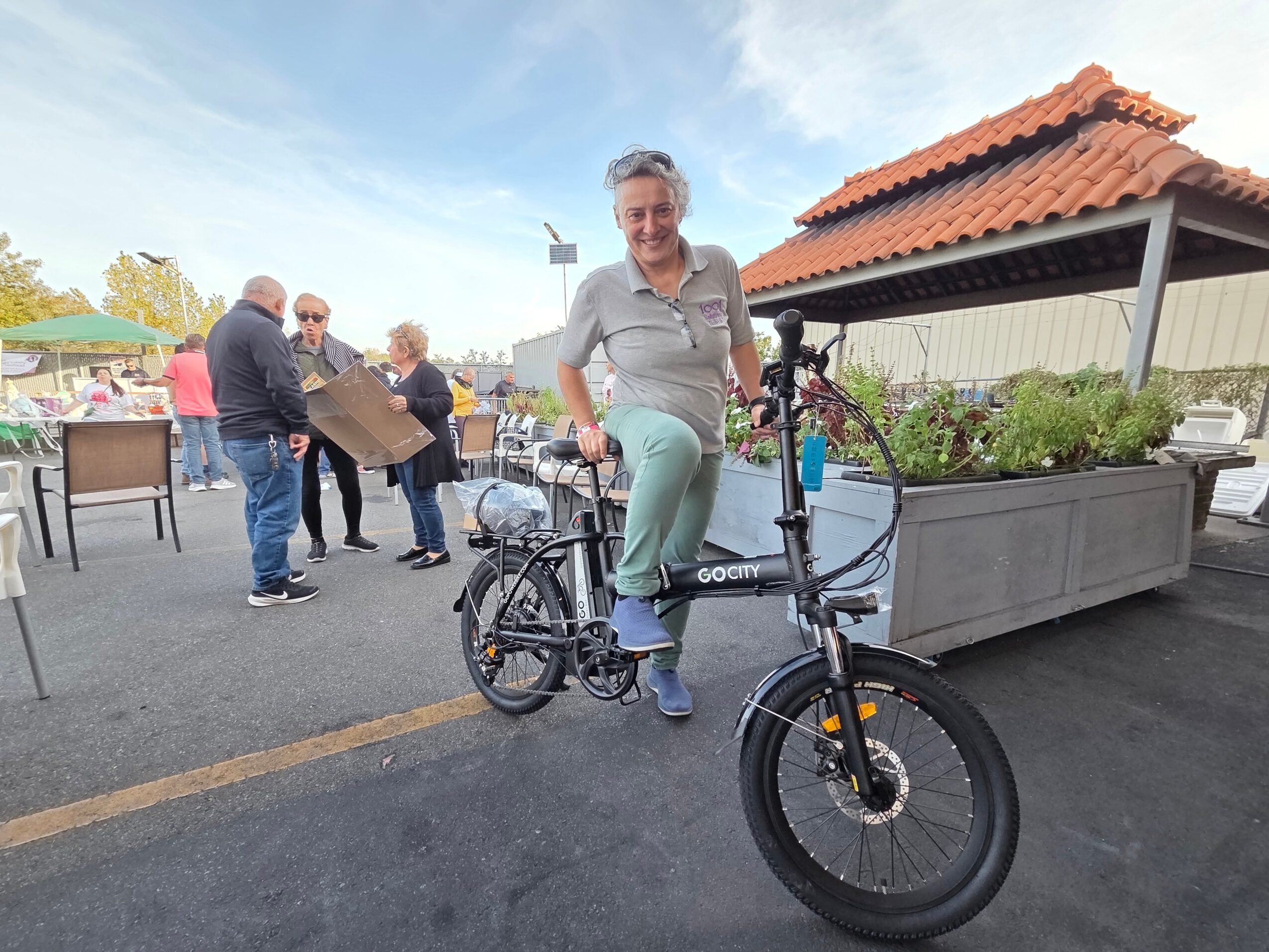 Person standing next to a black bicycle with a large planter box nearby, outdoors on a sunny day.
