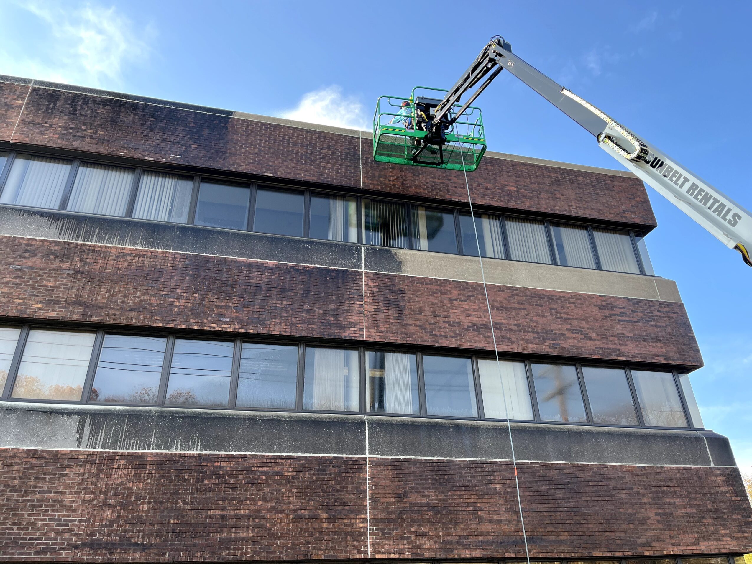 A building with a worker in a green lift cleaning windows, blue sky background.