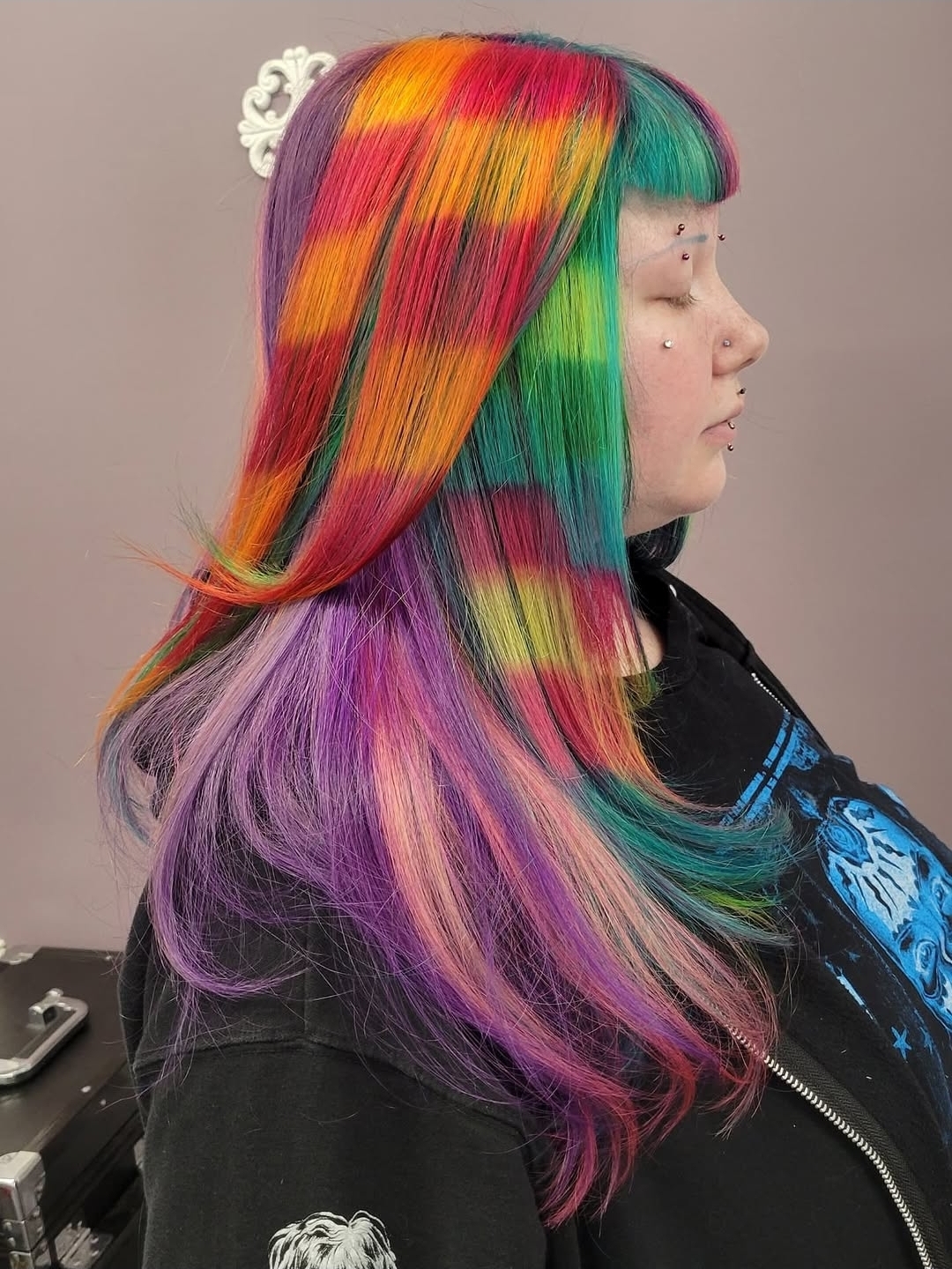 Profile of a person with long, rainbow-colored hair styled straight, with a white hair accessory, against a plain background.
