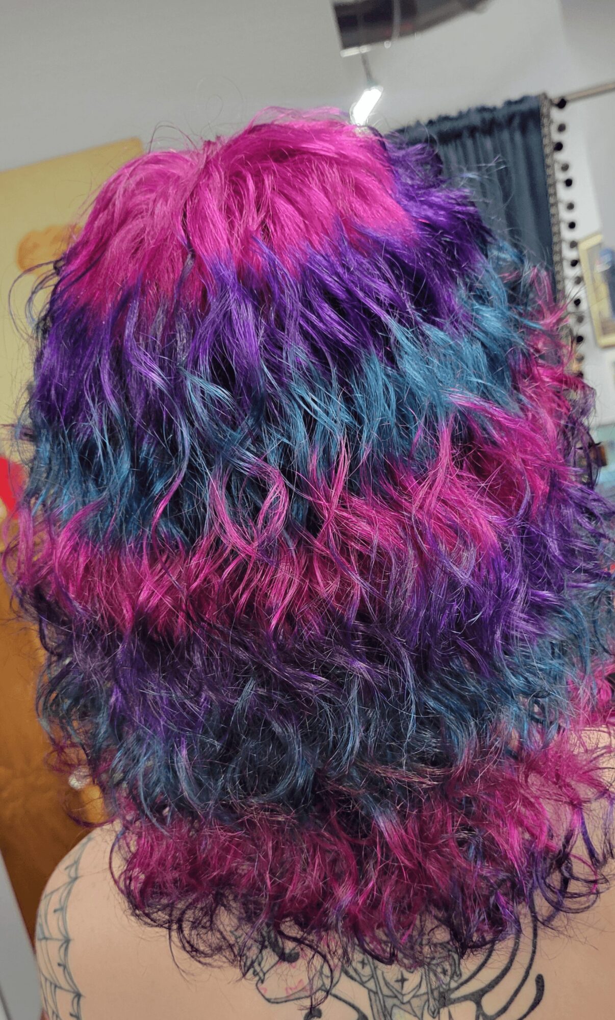 Back of a person with curly, multicolored hair in pink, purple, blue, and teal shades.