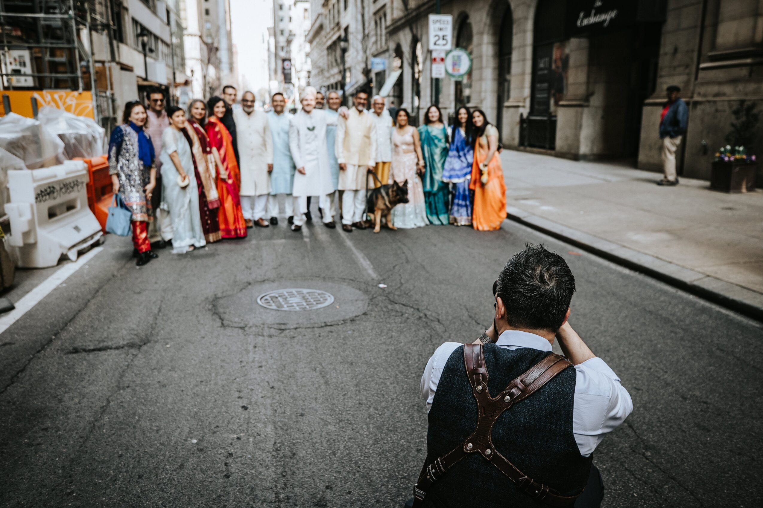 Group of people in colorful traditional clothing standing on a city street, with a person taking a photo in the foreground.