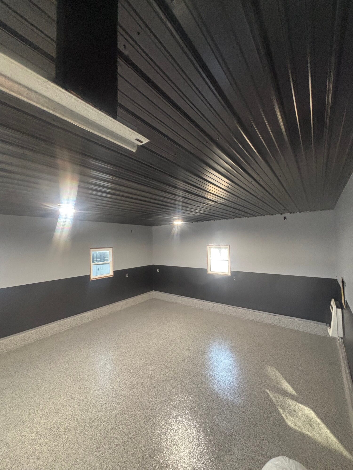Interior hallway with dark ceiling, light-colored floor, and bright lighting fixtures, including a window and a door.